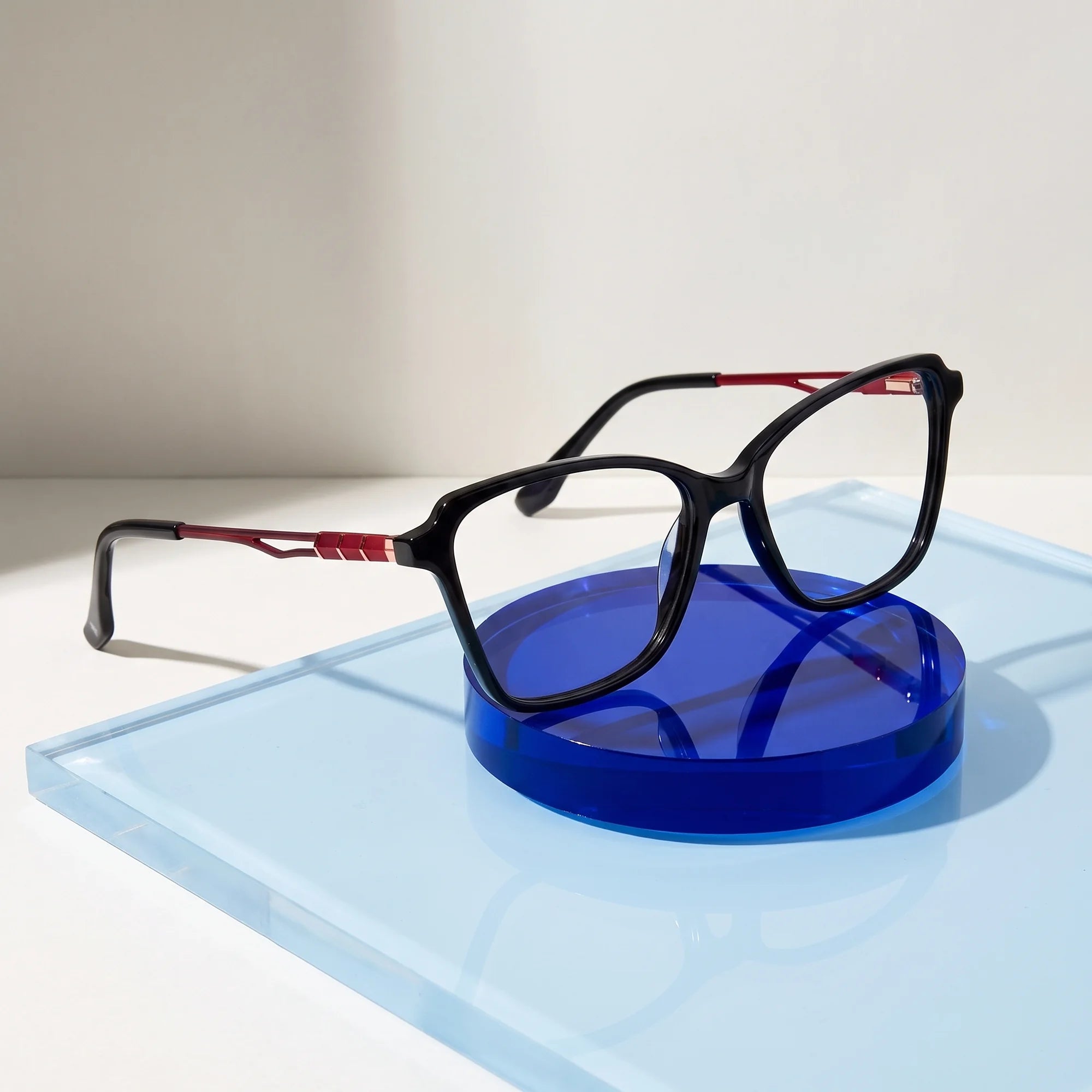 Fiore 1006 eyeglasses in black – on a cobalt acrylic disc in soft daylight