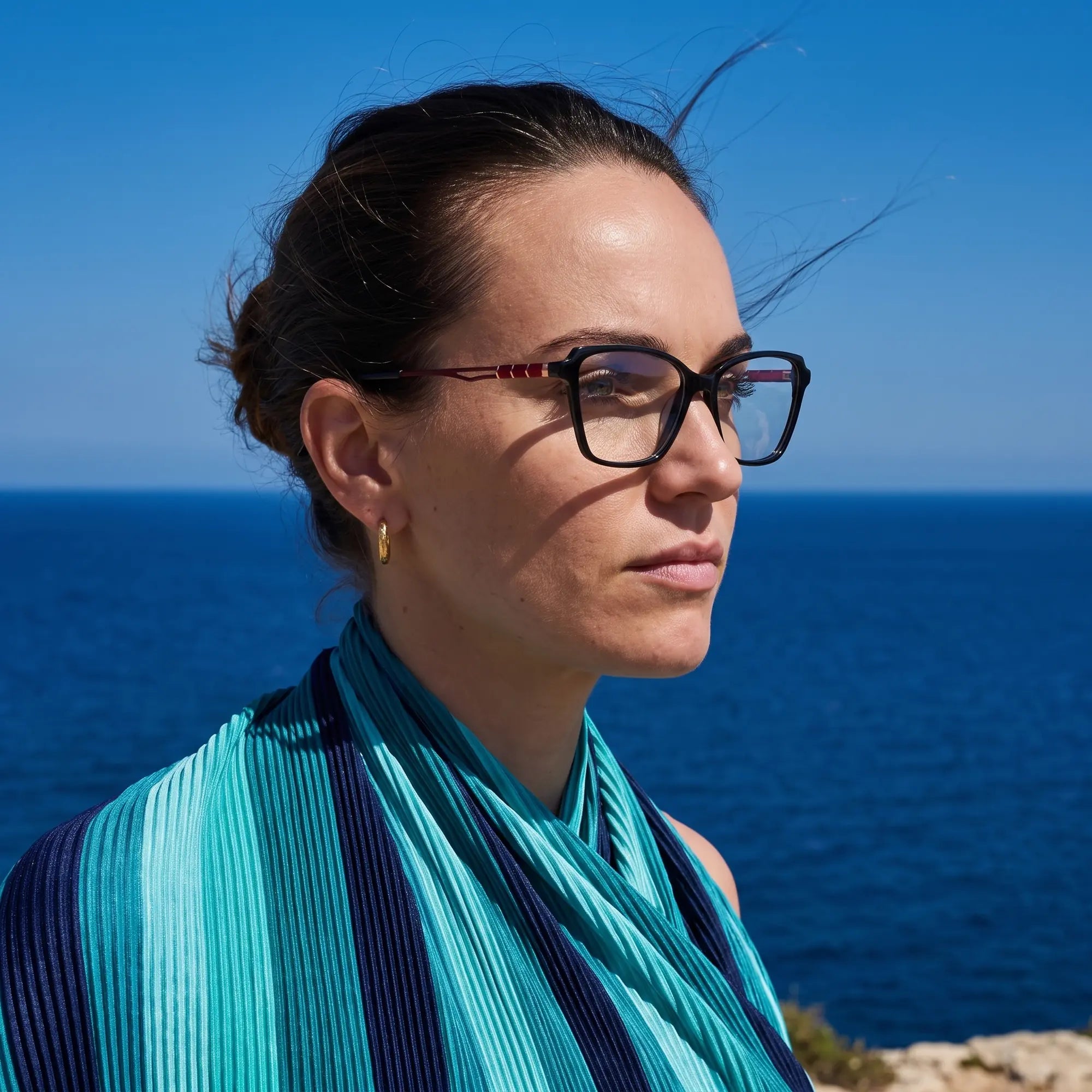 Fiore 1006 eyeglasses in black, worn by a model – campaign portrait, windswept portrait over the deep blue sea