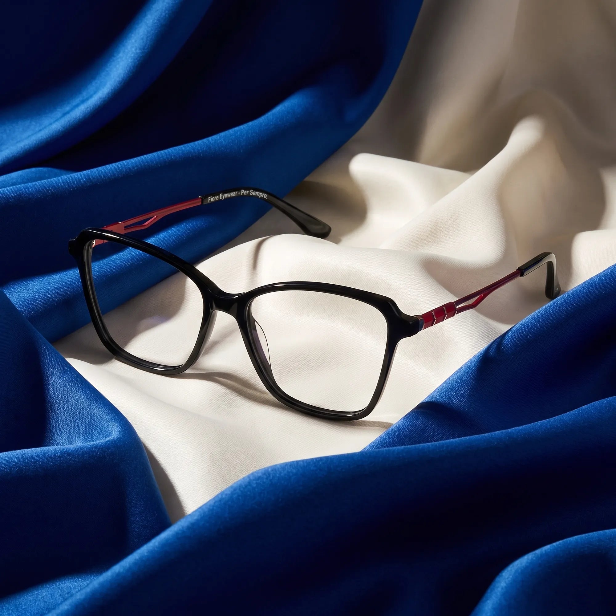 Fiore 1006 eyeglasses in black – resting on draped cobalt and ivory silk