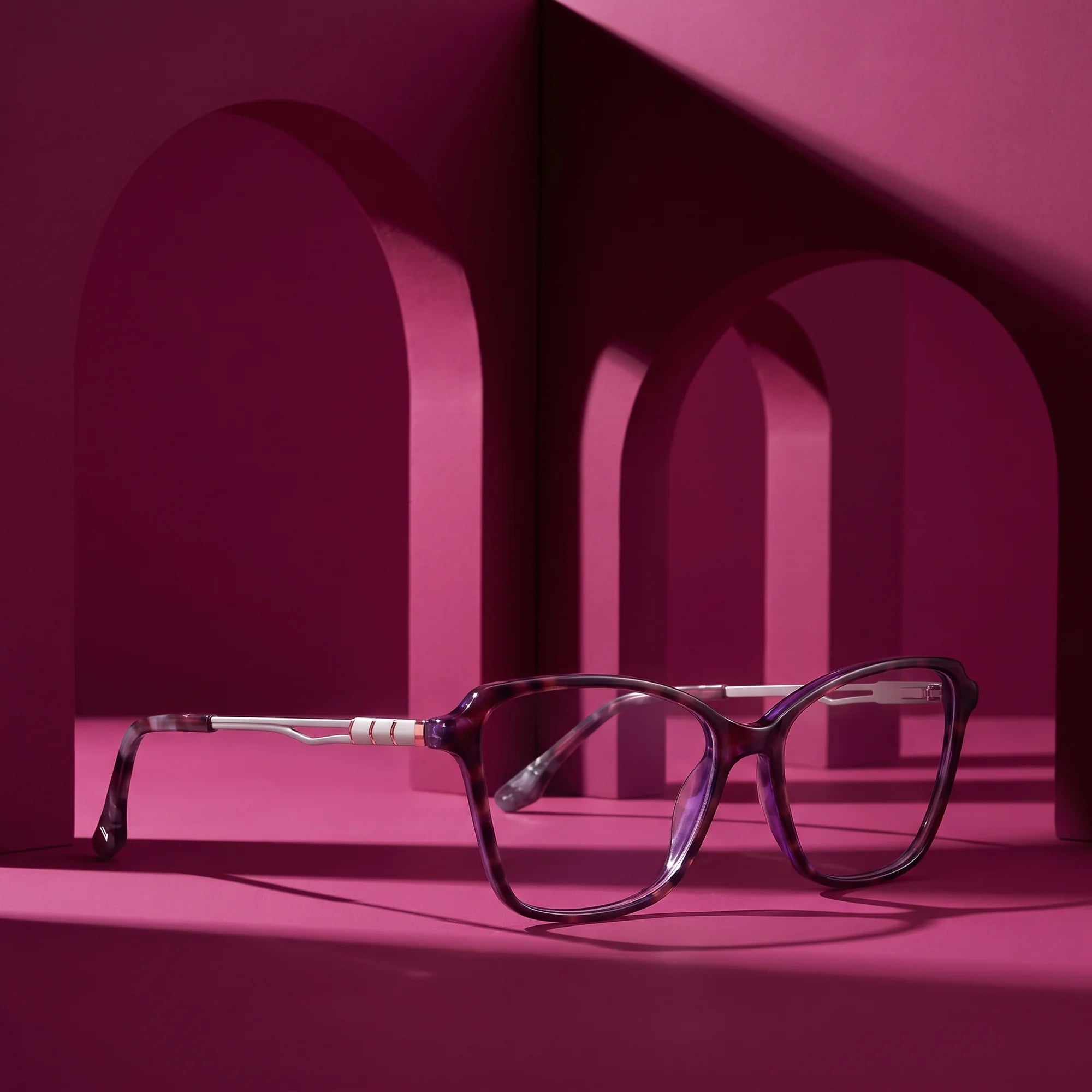 Fiore 1006 eyeglasses in purple – displayed on a magenta podium among arches