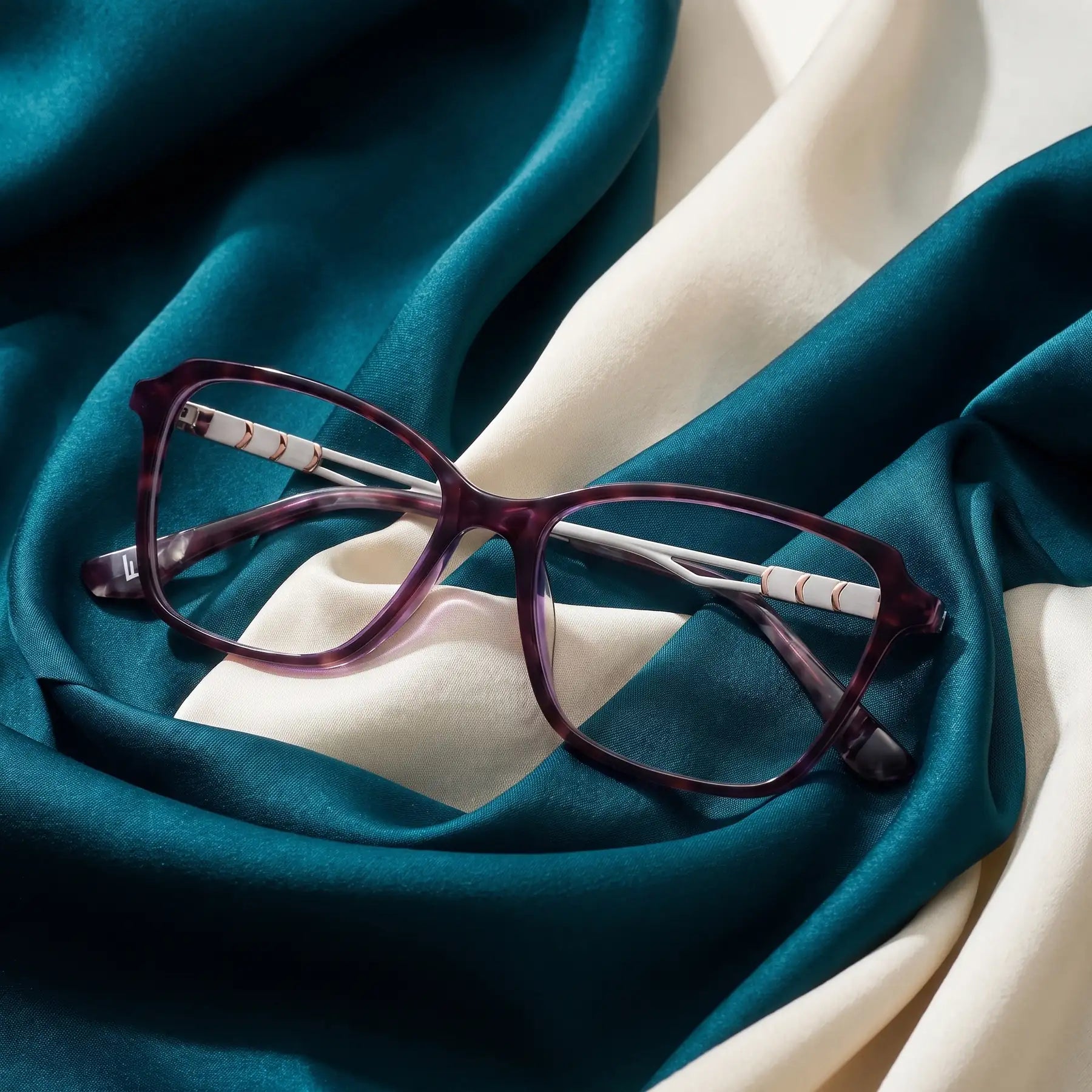 Fiore 1006 eyeglasses in purple – resting on draped teal and ivory silk