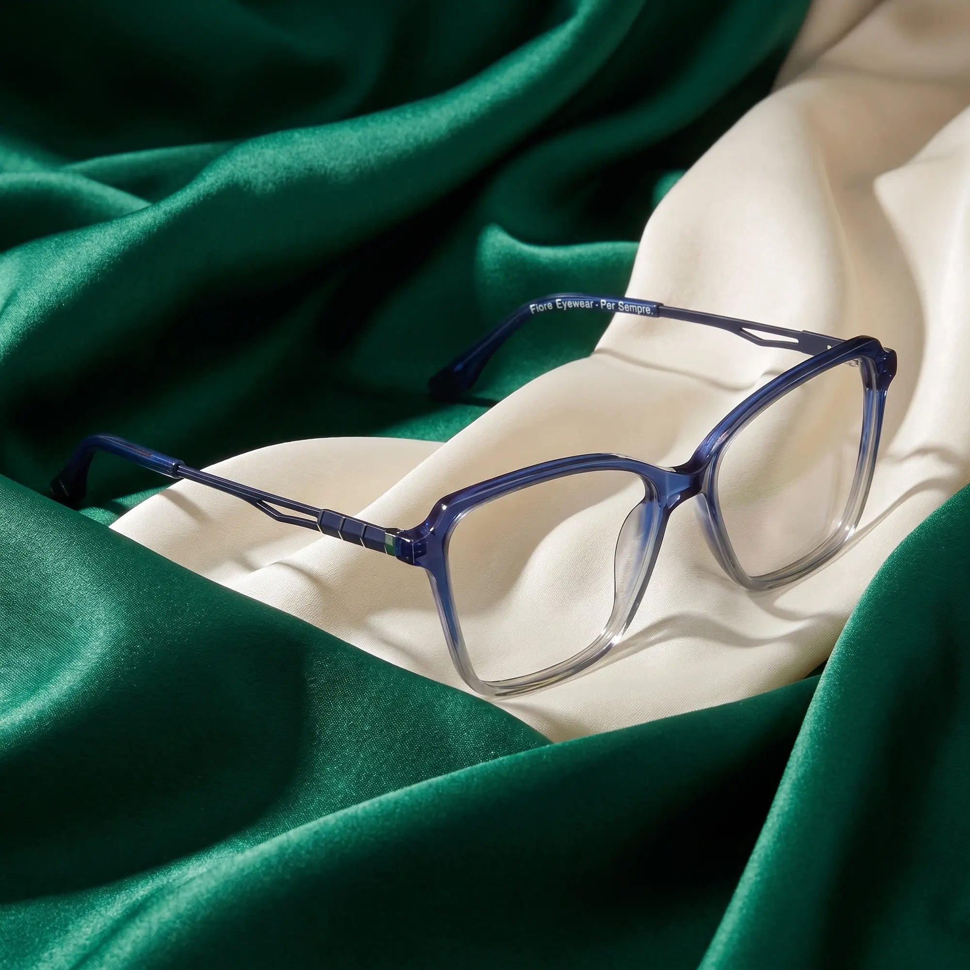Fiore 1006 eyeglasses in blue – resting on draped emerald and ivory silk