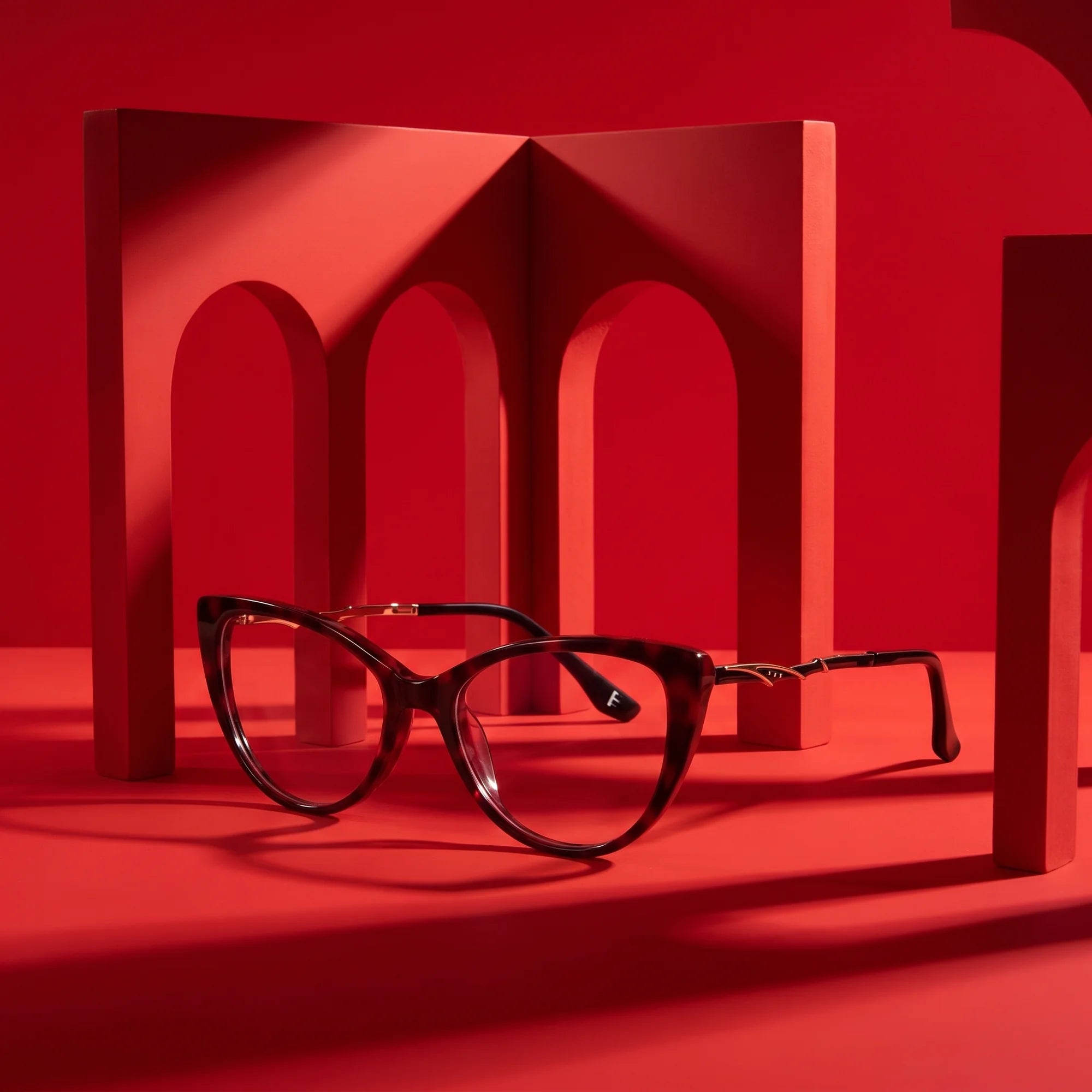 Fiore 1010 eyeglasses in red – displayed on a vivid red podium among arches