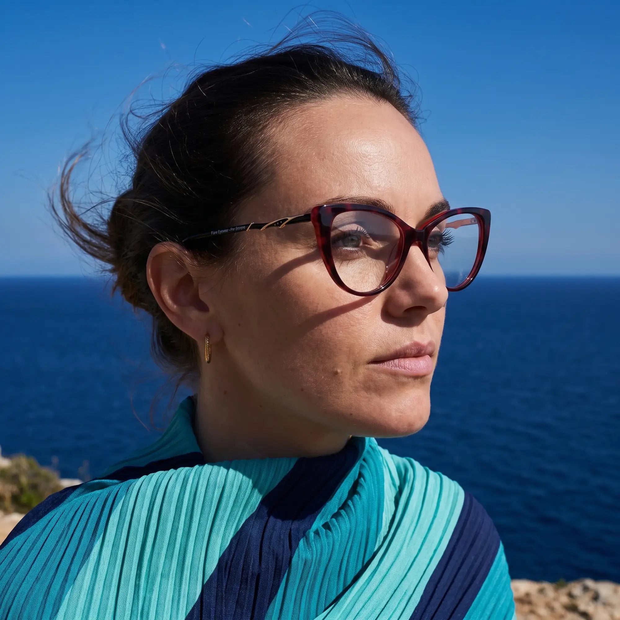 Fiore 1010 eyeglasses in red, worn by a model – campaign portrait, windswept portrait over the deep blue sea