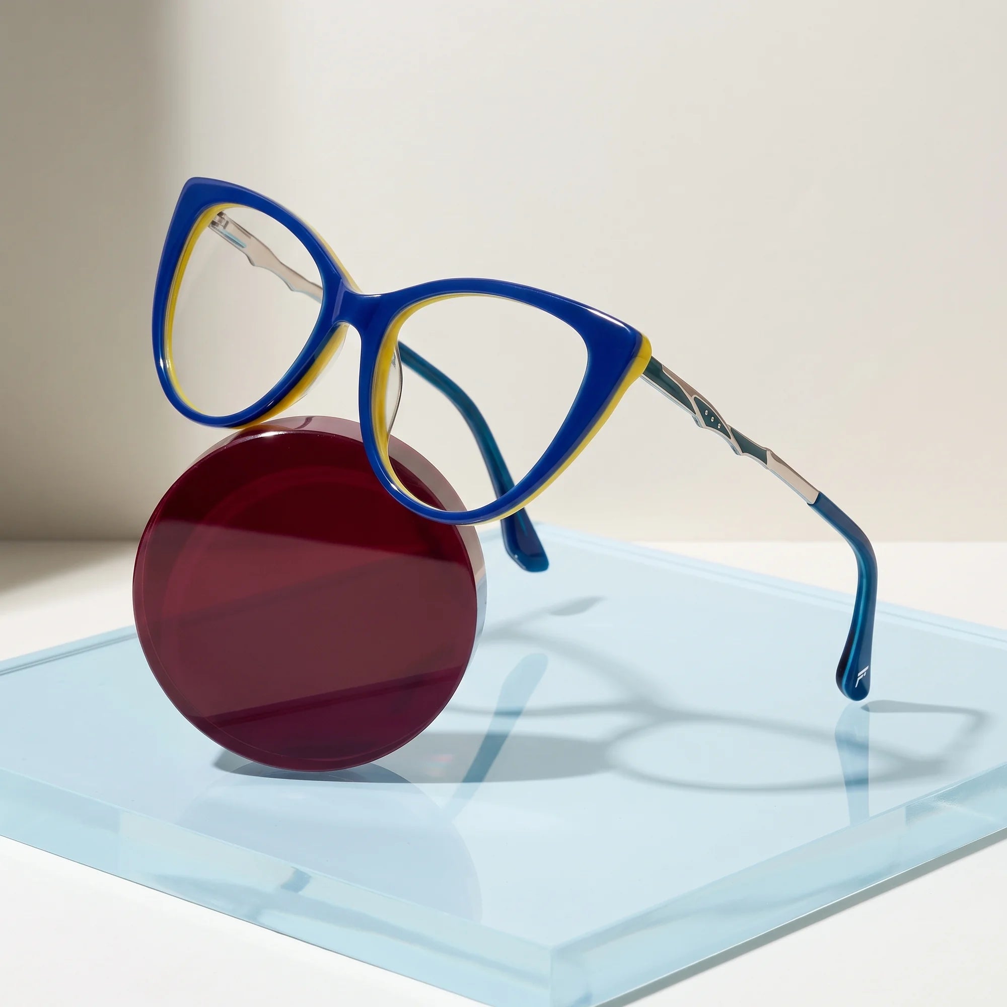 Fiore 1010 eyeglasses in blue green – on a cobalt acrylic disc in soft daylight