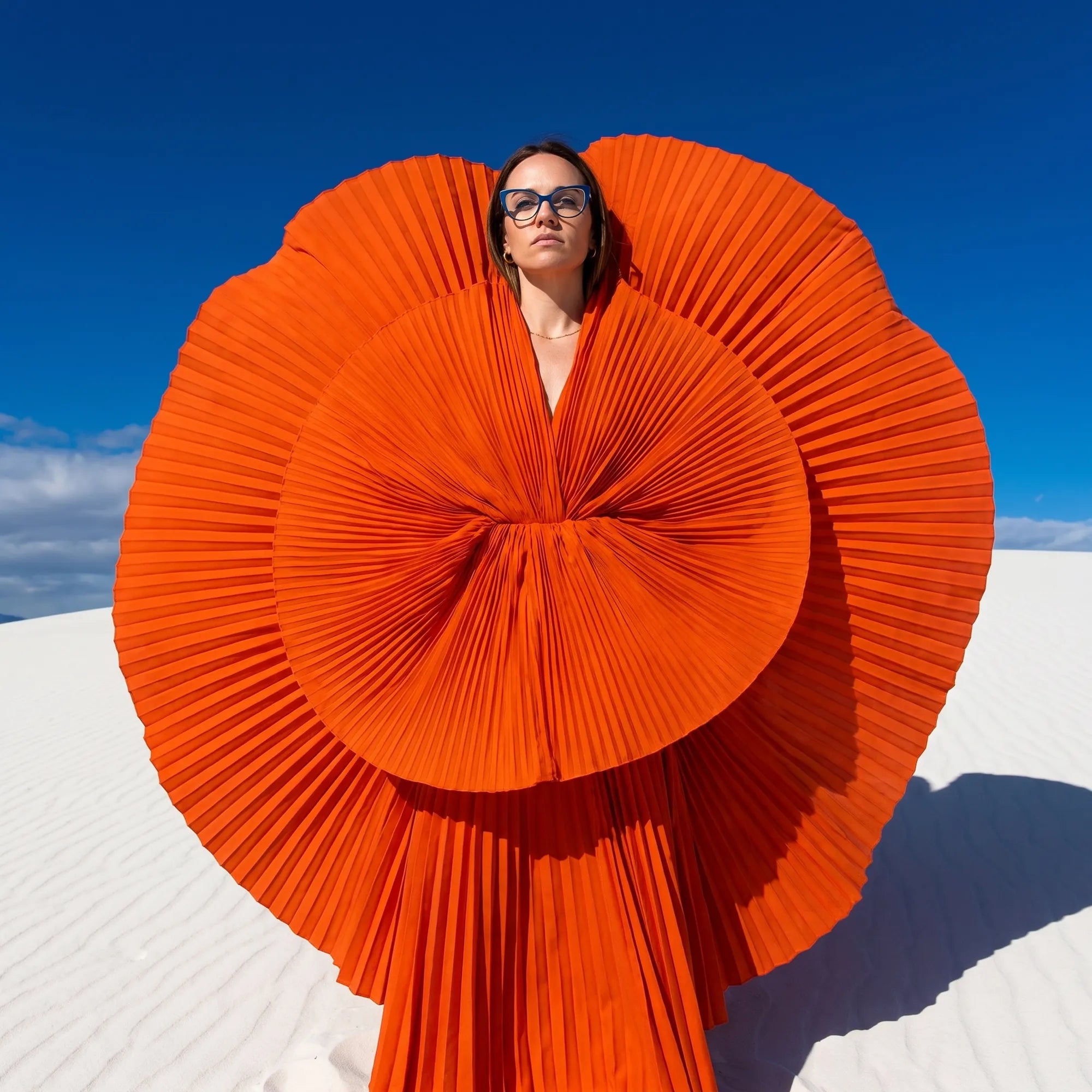 Fiore 1010 eyeglasses in blue green, worn by a model – campaign portrait, sculptural orange pleated fan on white dunes