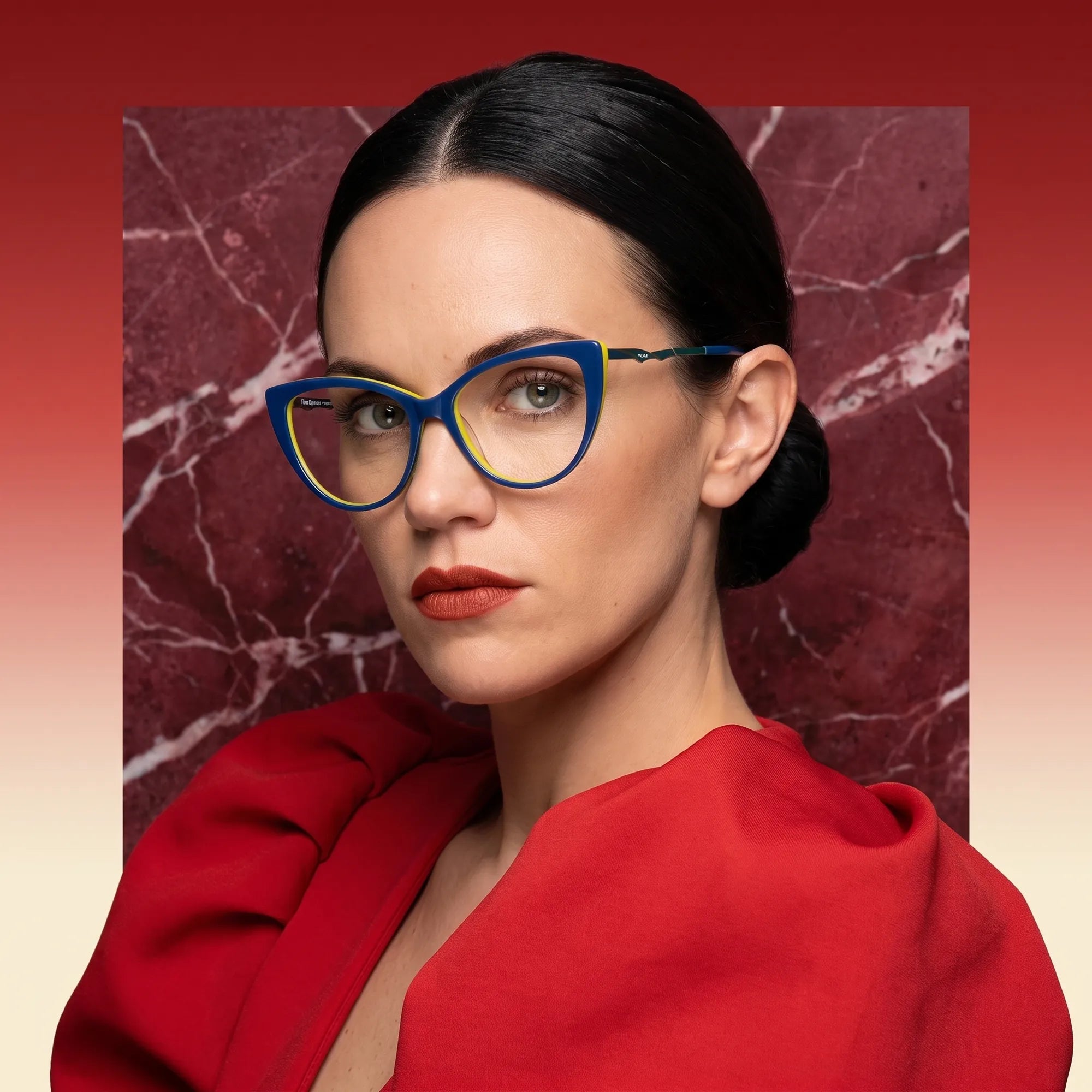 Fiore 1010 eyeglasses in blue green, worn by a model – campaign portrait, red marble backdrop and draped scarlet dress