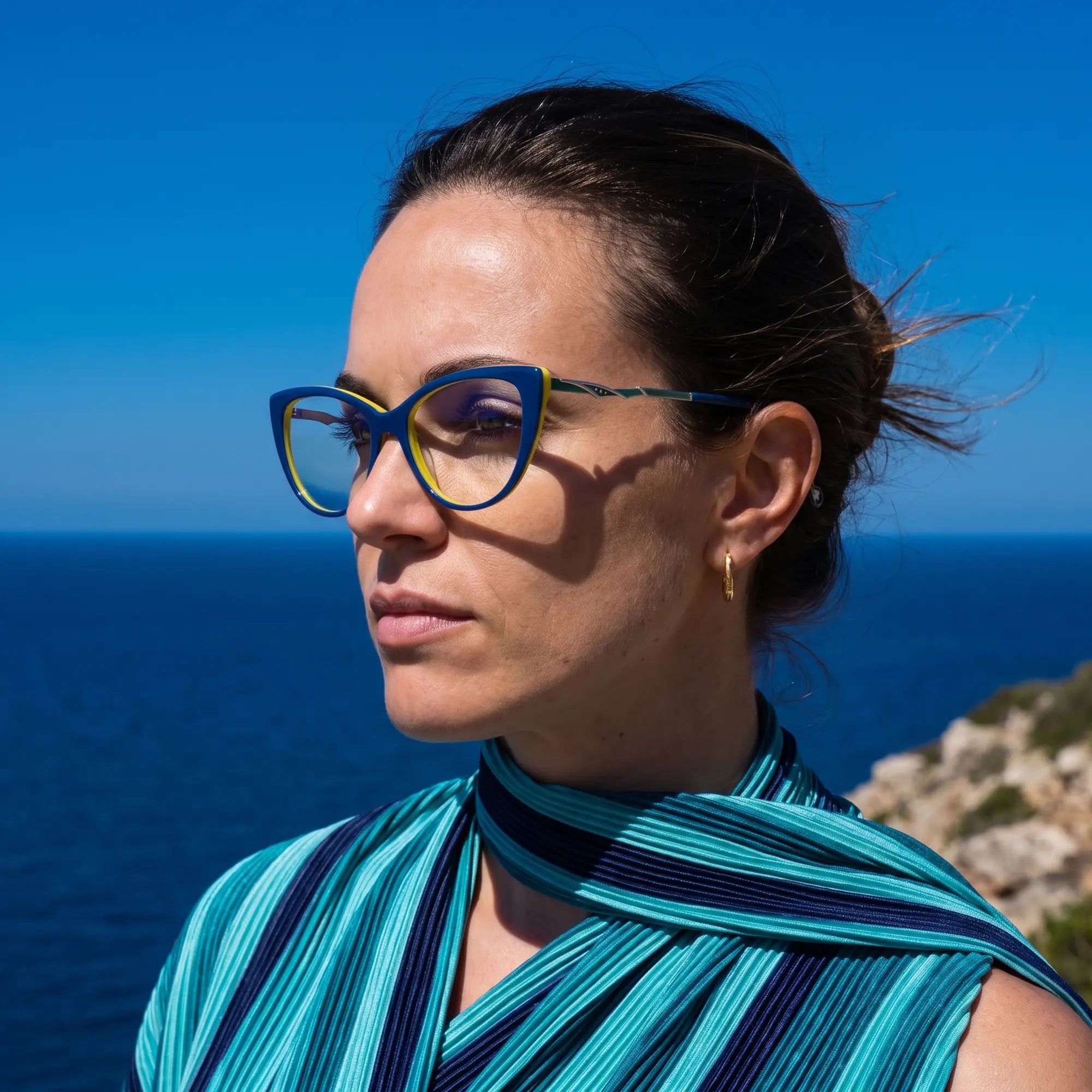 Fiore 1010 eyeglasses in blue green, worn by a model – campaign portrait, windswept portrait over the deep blue sea