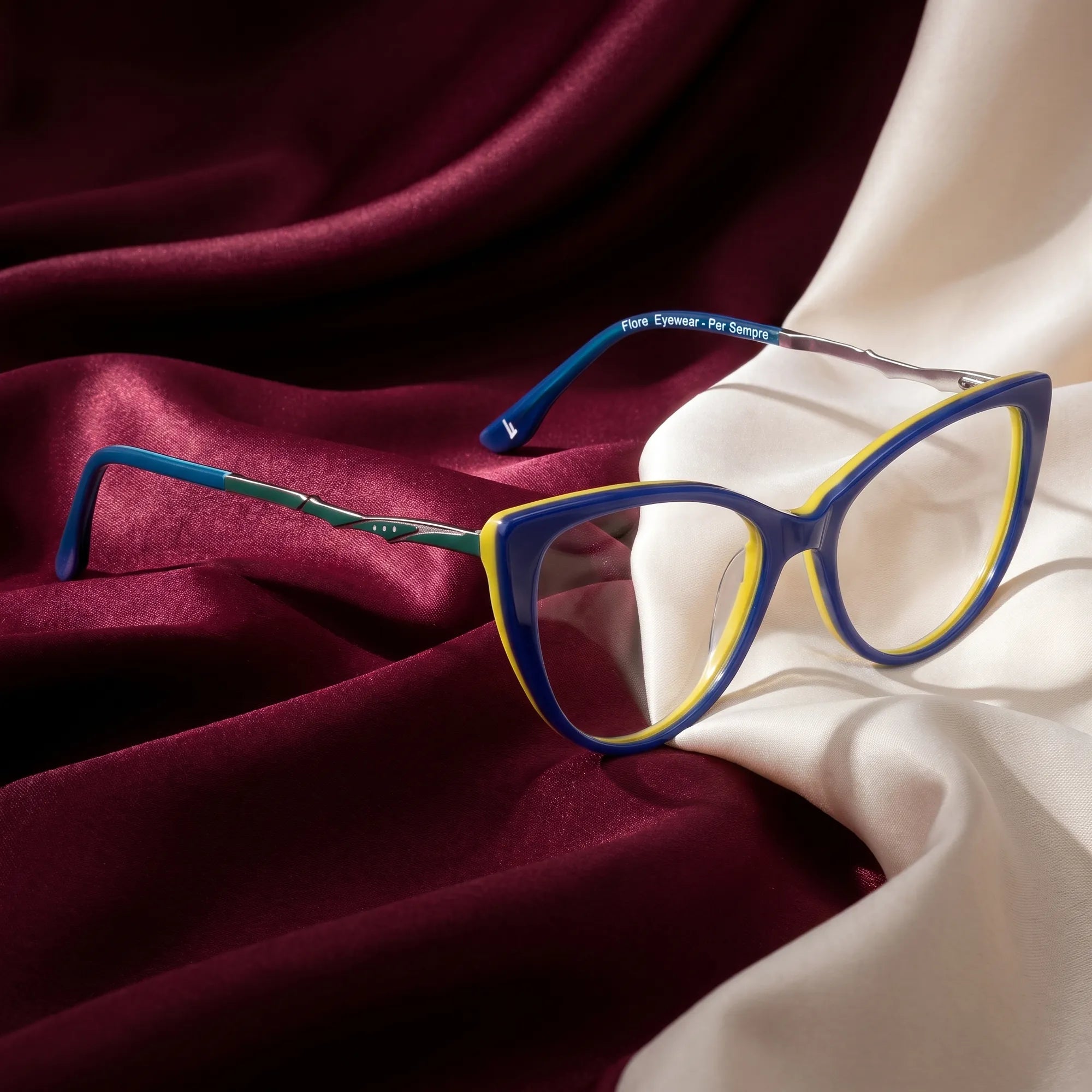 Fiore 1010 eyeglasses in blue green – resting on draped burgundy and ivory silk