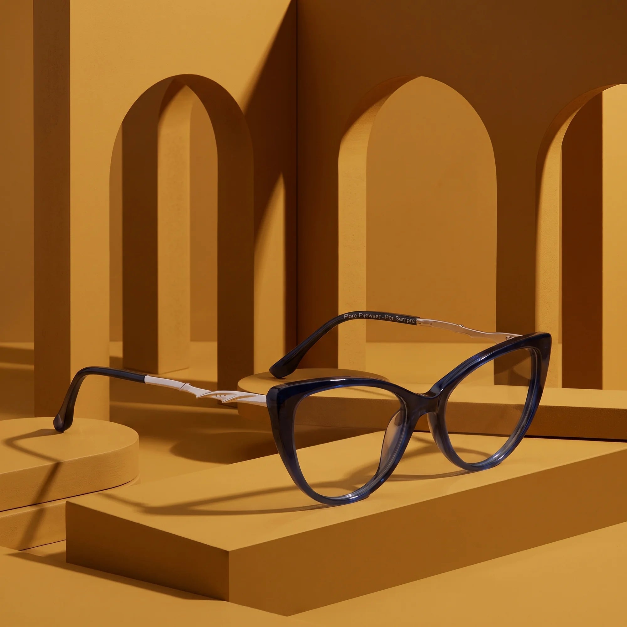 Fiore 1010 eyeglasses in blue – displayed on a mustard ochre podium among arches