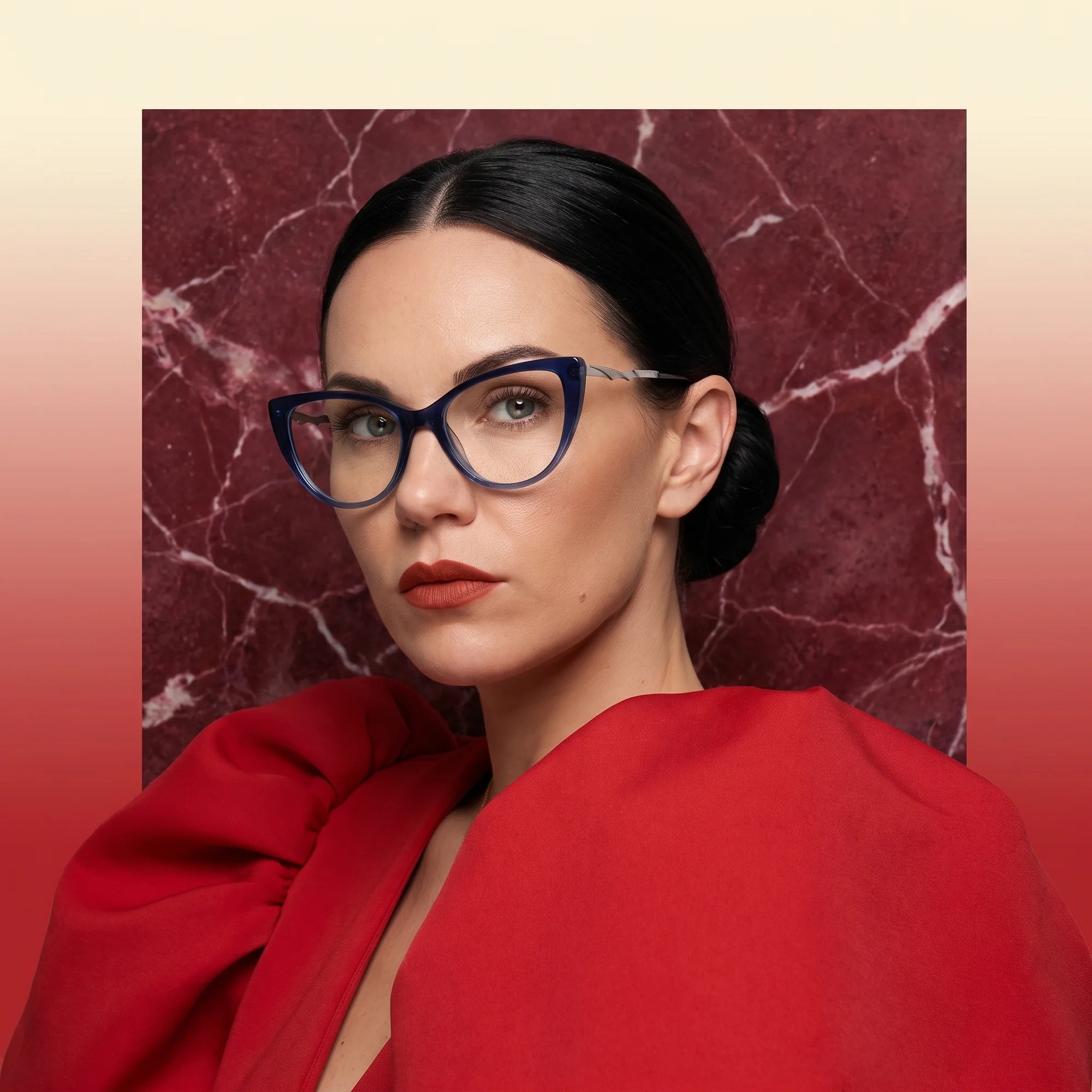 Fiore 1010 eyeglasses in blue, worn by a model – campaign portrait, red marble backdrop and draped scarlet dress