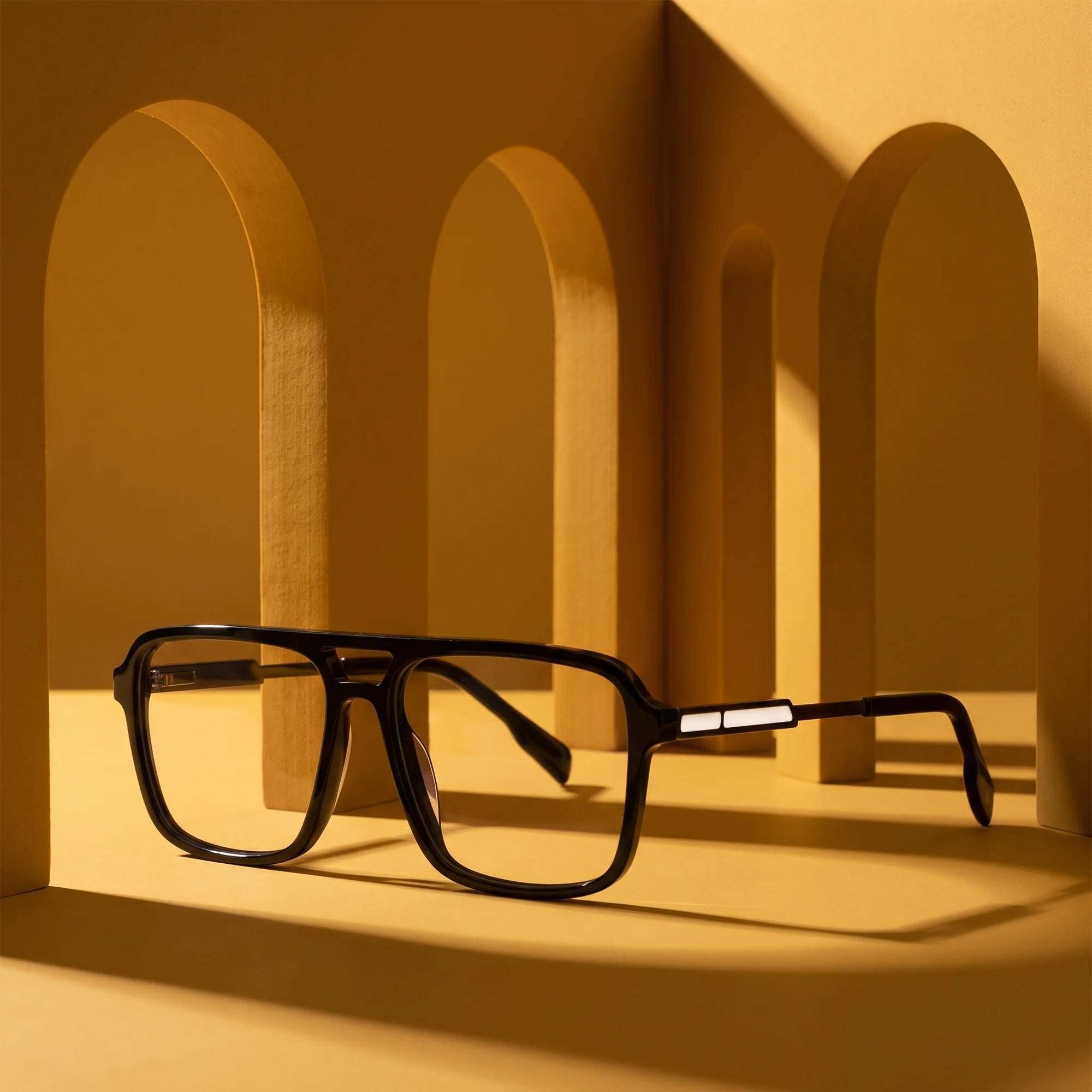Fiore 1014 eyeglasses in black – displayed on a mustard ochre podium among arches