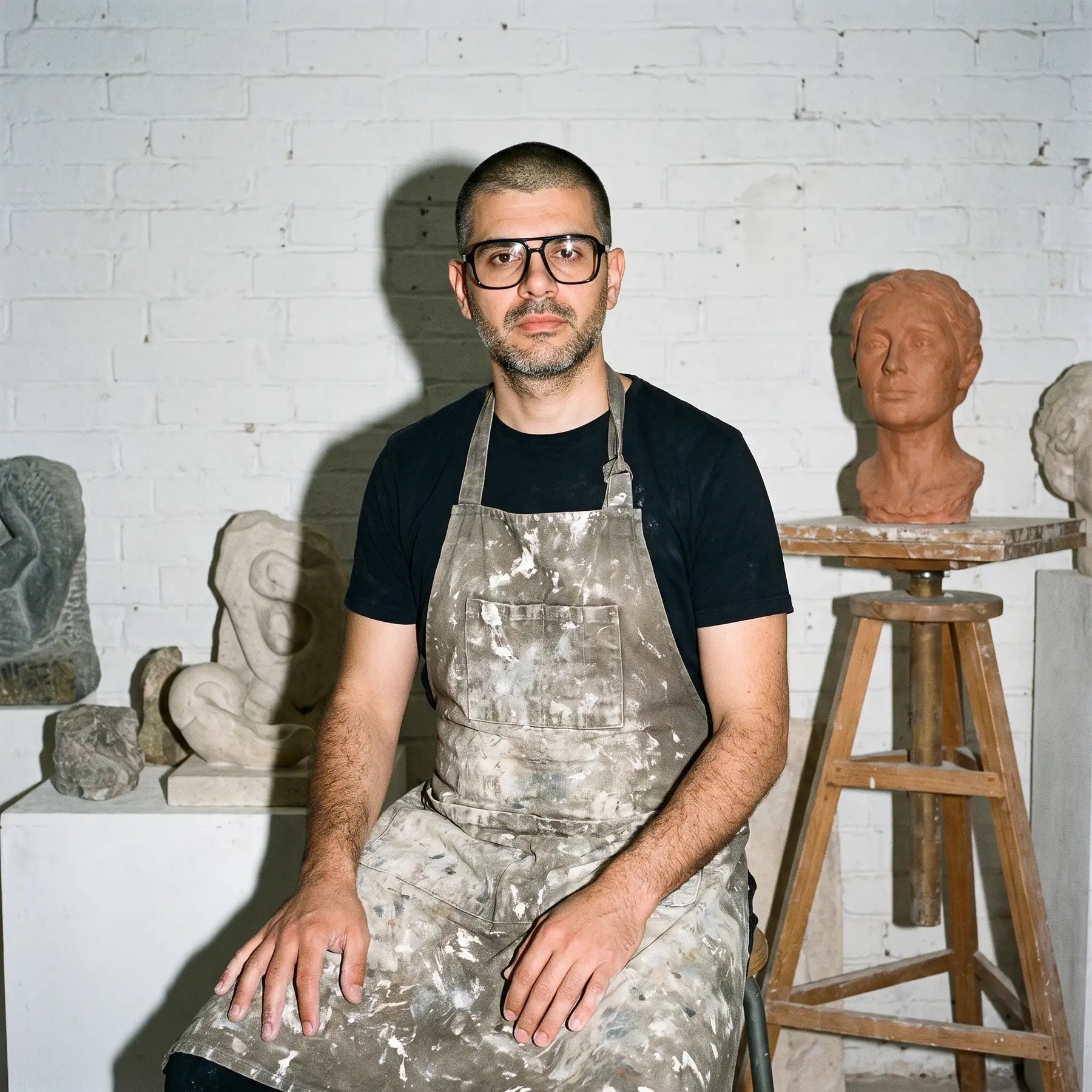 Fiore 1014 eyeglasses in black, worn by a model – campaign portrait, sculptor portrait among clay busts in a workshop