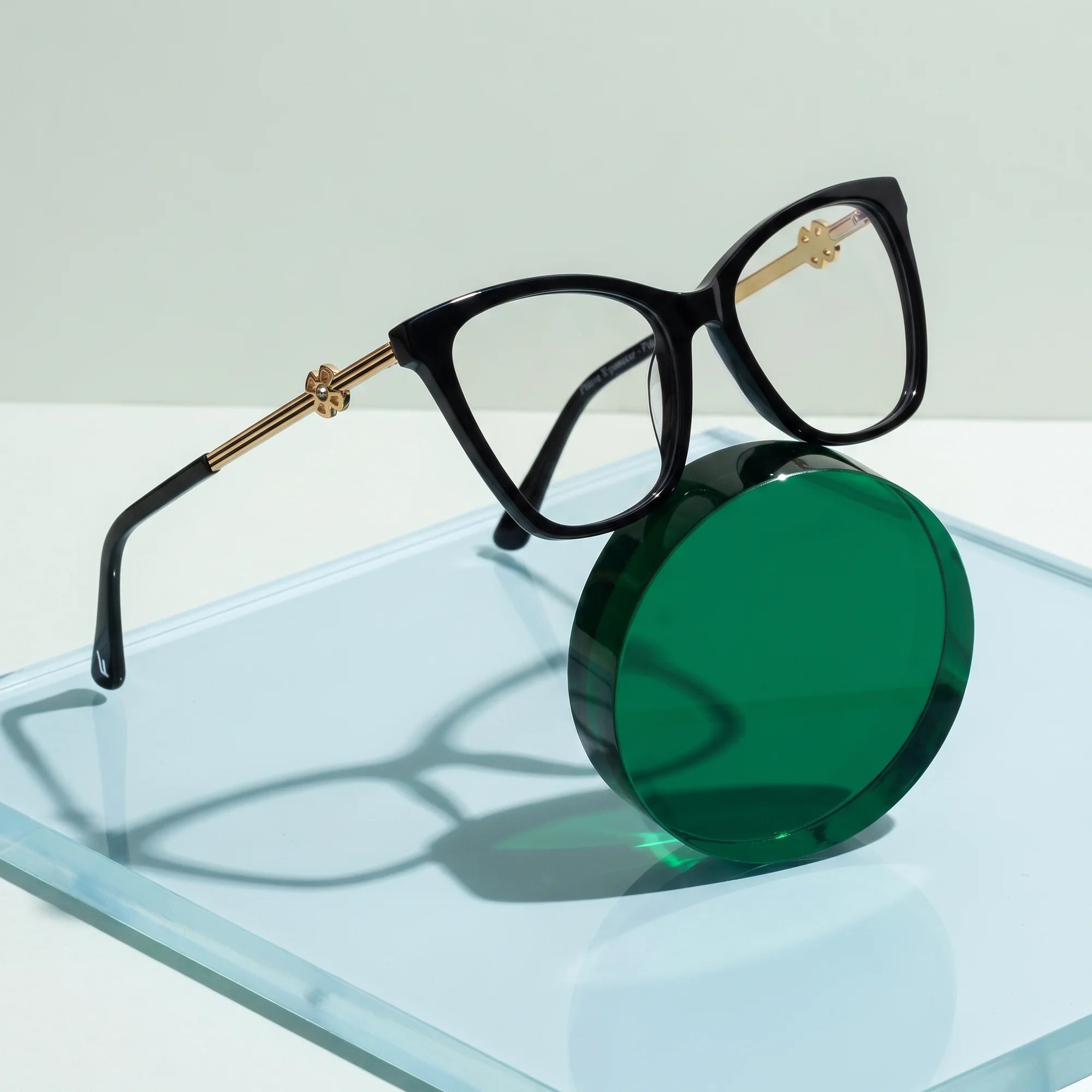 Fiore 10172 eyeglasses in black – on a cobalt acrylic disc in soft daylight