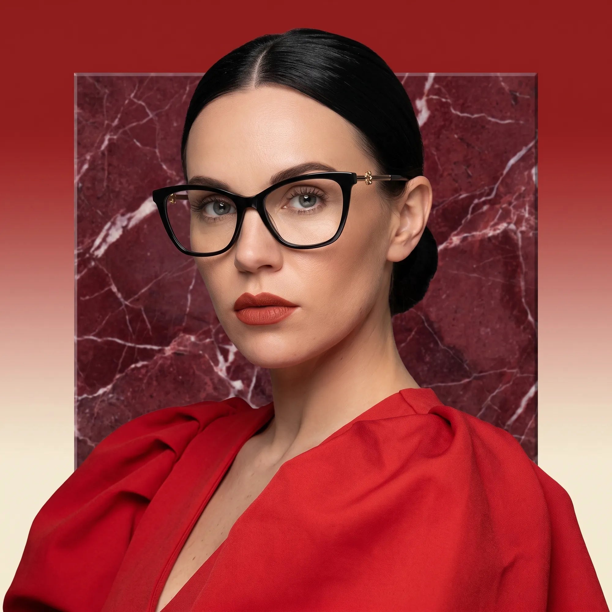Fiore 10172 eyeglasses in black, worn by a model – campaign portrait, red marble backdrop and draped scarlet dress