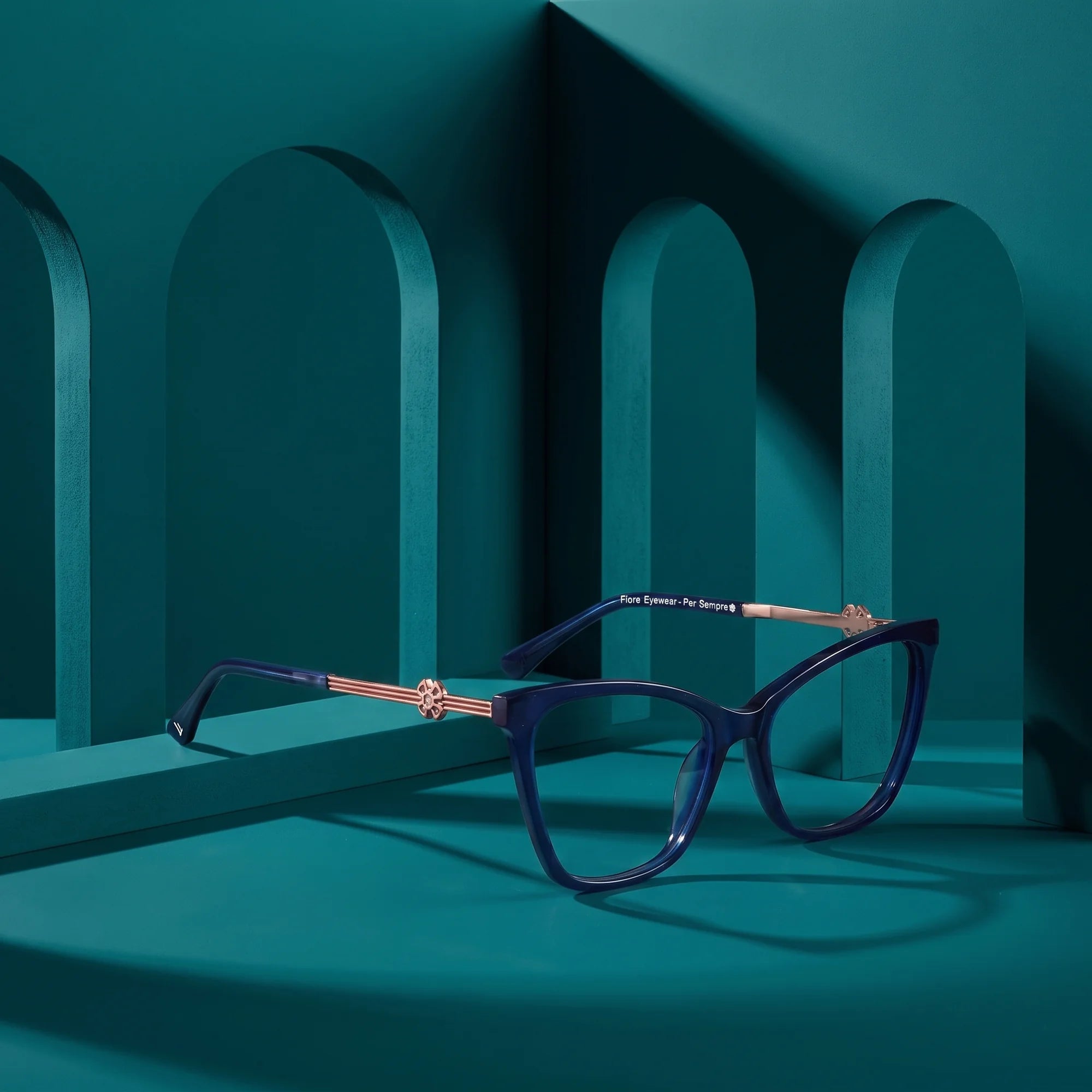 Fiore 10172 eyeglasses in blue – displayed on a teal podium among arches