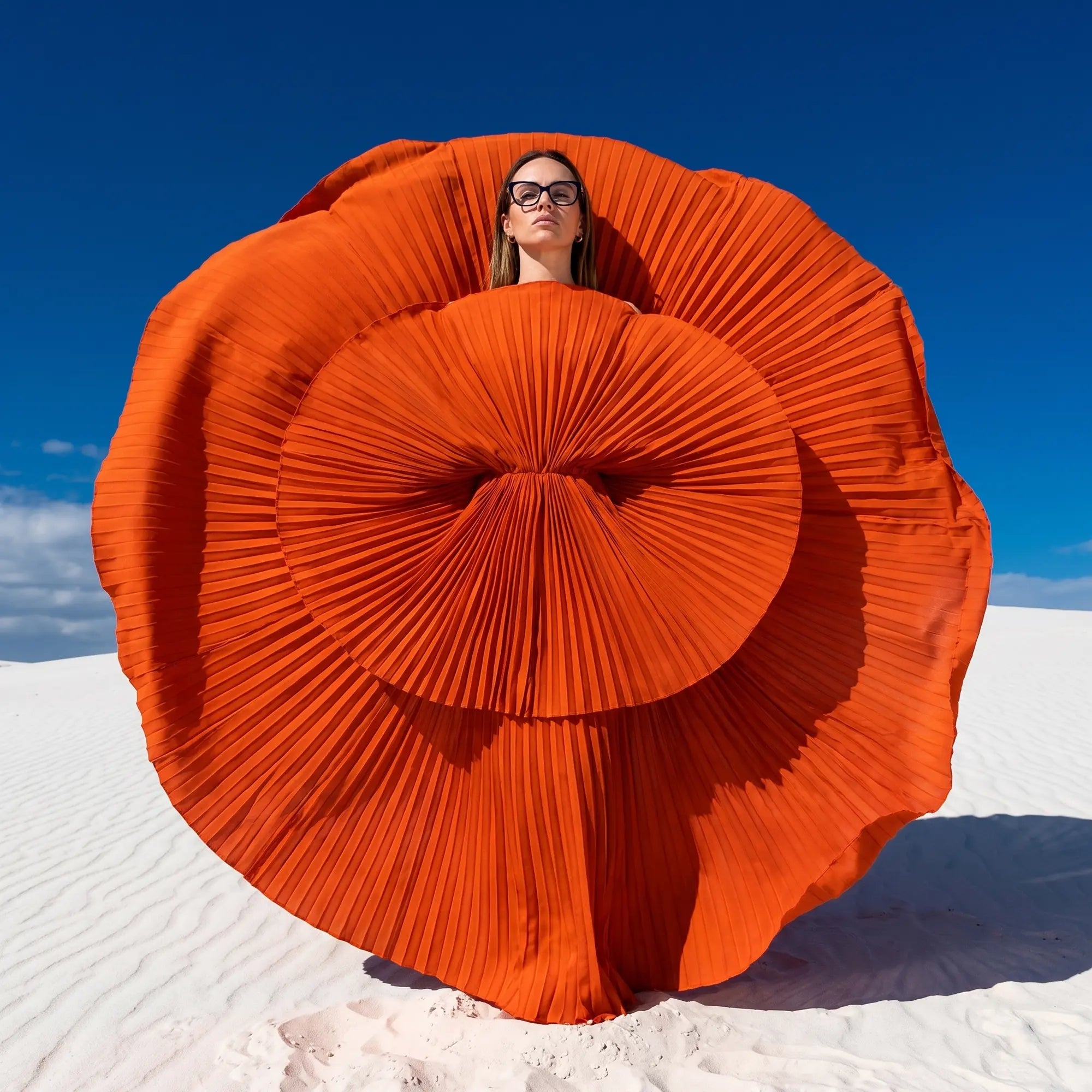Fiore 10172 eyeglasses in blue, worn by a model – campaign portrait, sculptural orange pleated fan on white dunes