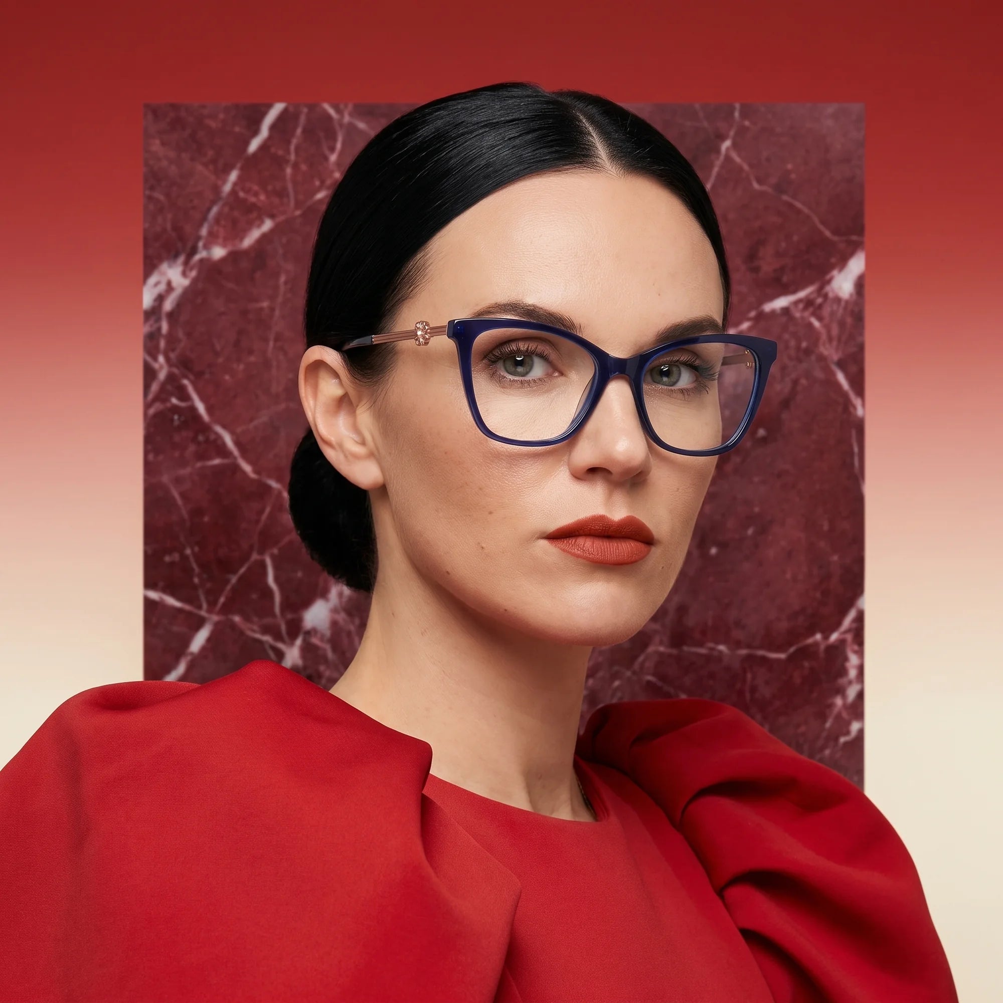 Fiore 10172 eyeglasses in blue, worn by a model – campaign portrait, red marble backdrop and draped scarlet dress