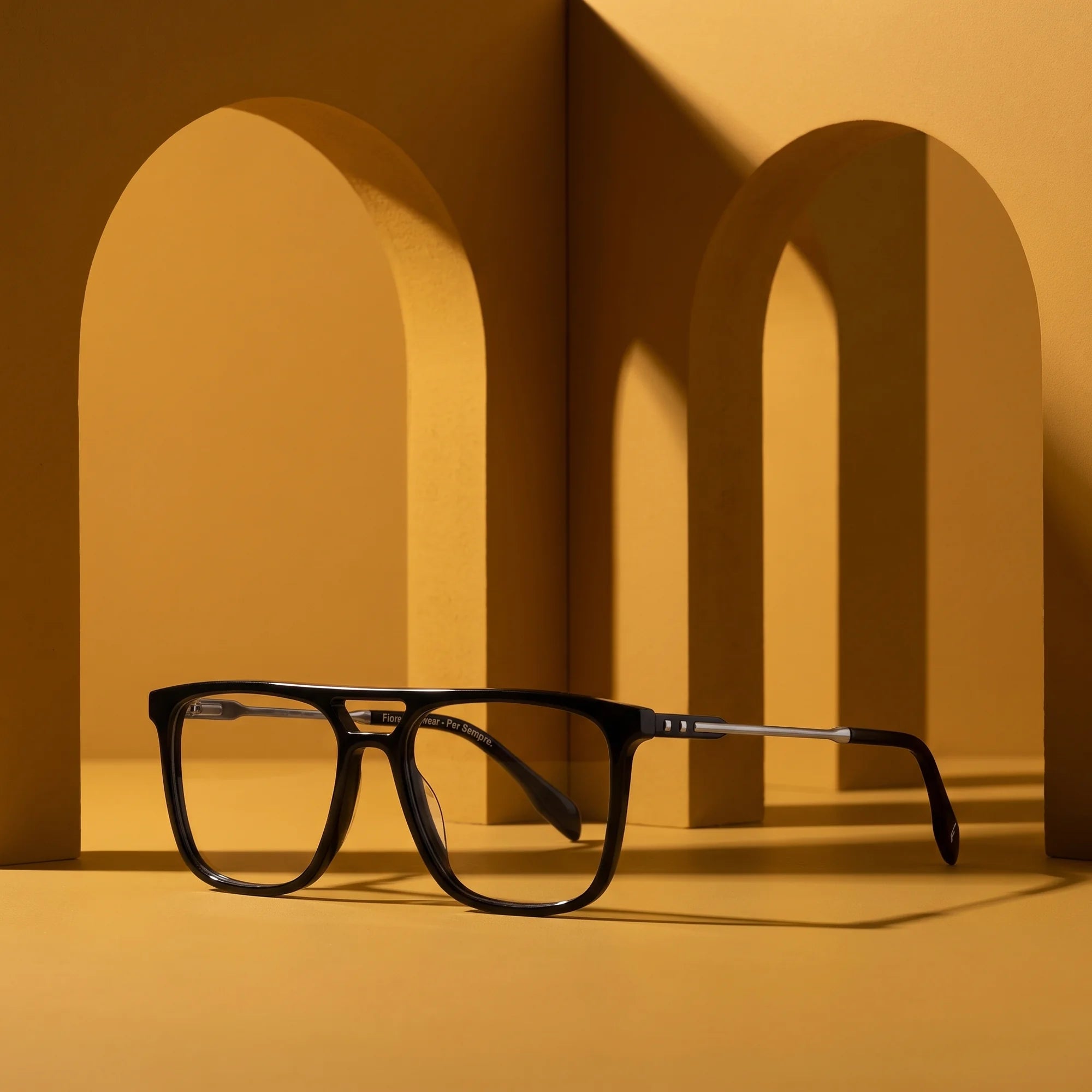Fiore 10177 eyeglasses in black – displayed on a mustard ochre podium among arches