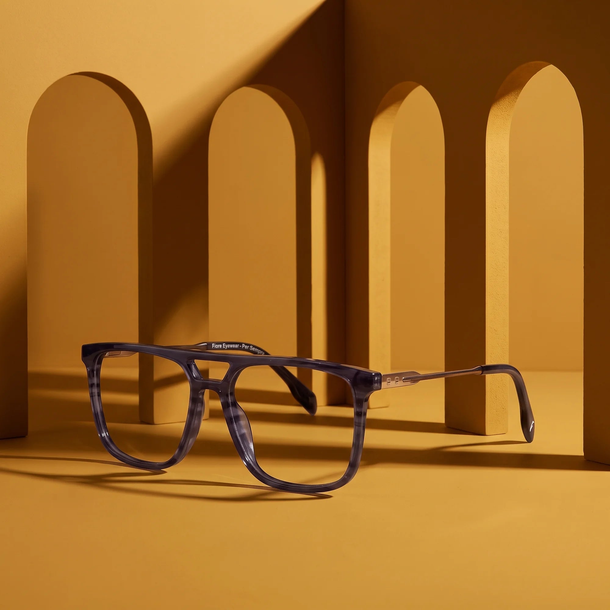 Fiore 10177 eyeglasses in grey – displayed on a mustard ochre podium among arches