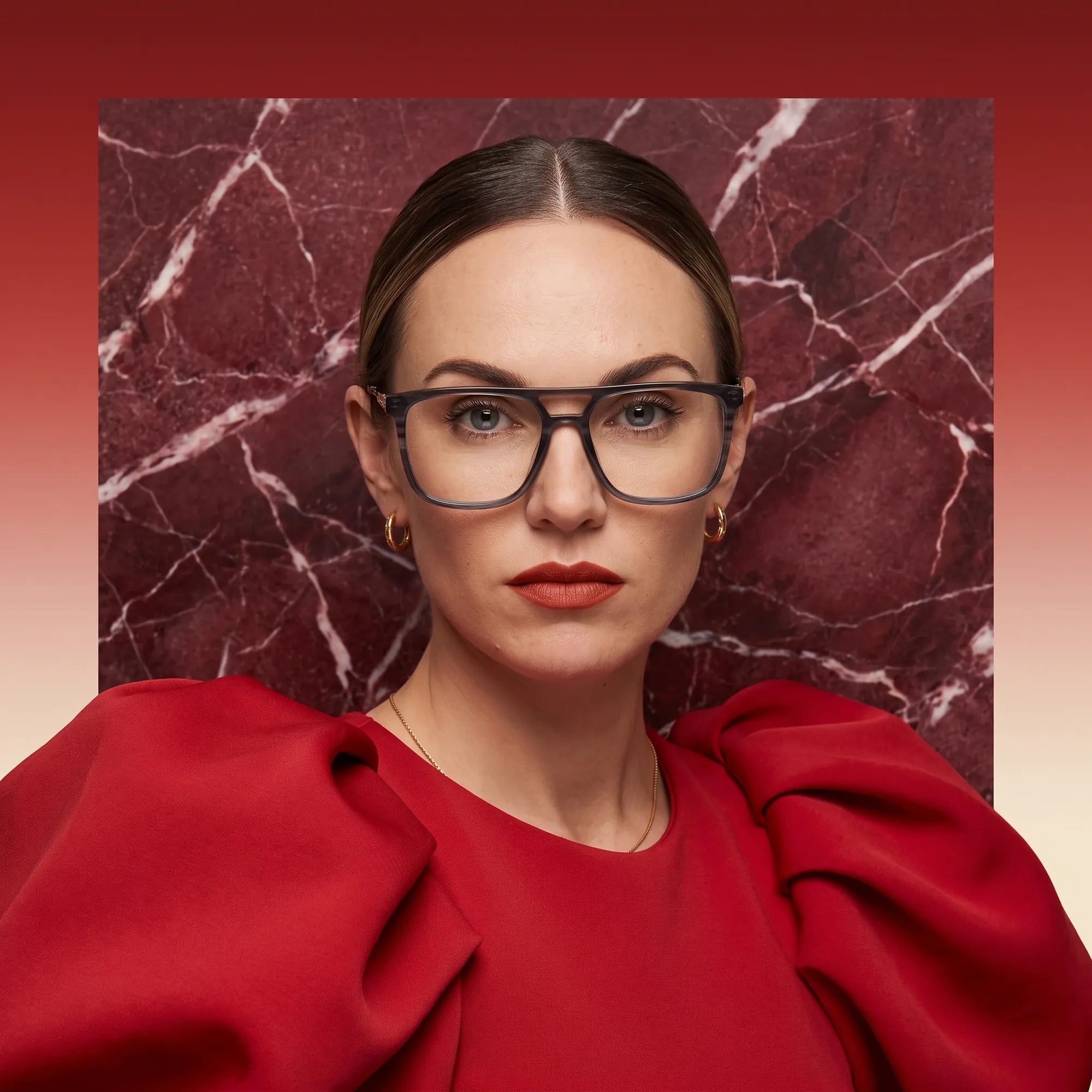 Fiore 10177 eyeglasses in grey, worn by a model – campaign portrait, red marble backdrop and draped scarlet dress