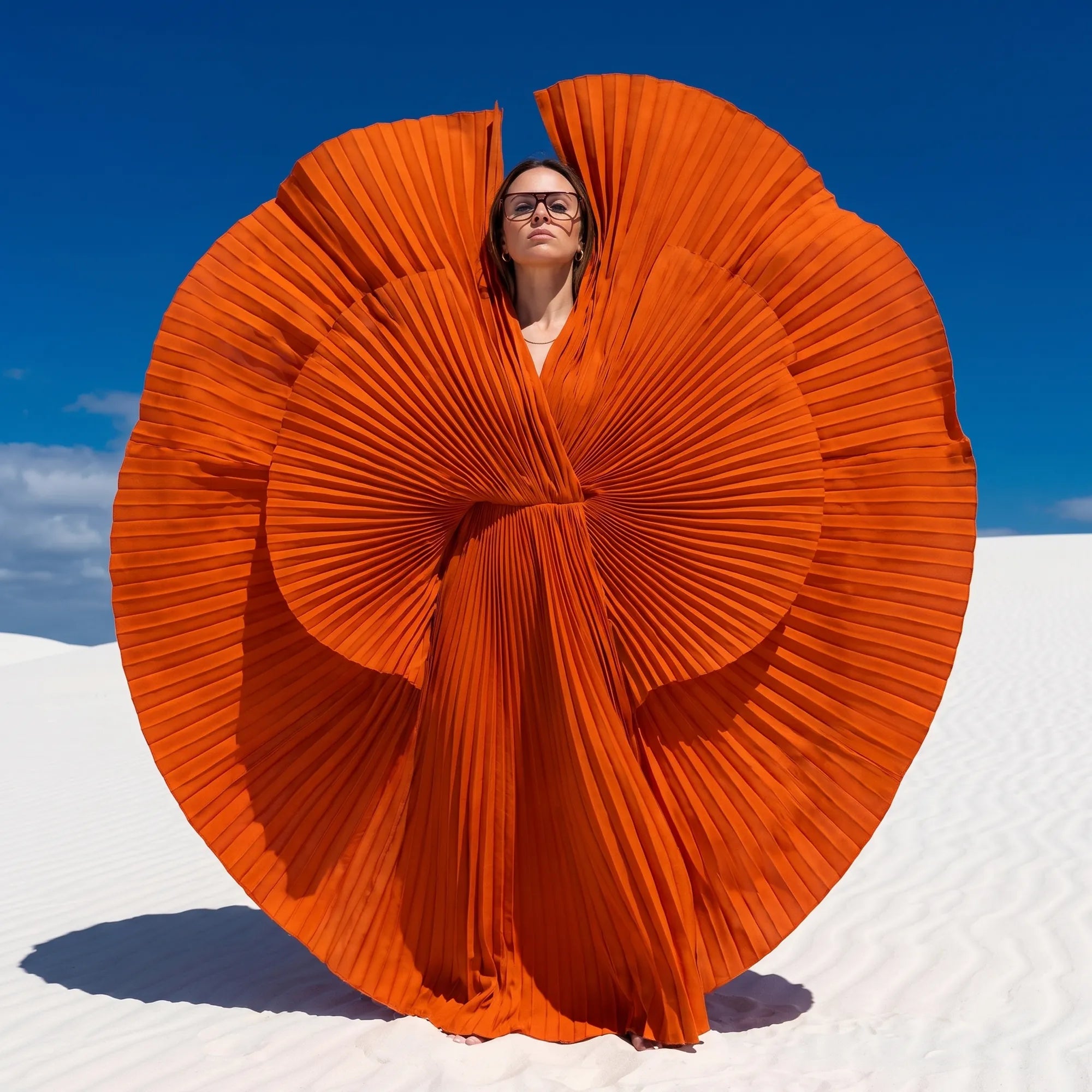 Fiore 10177 eyeglasses in brown, worn by a model – campaign portrait, sculptural orange pleated fan on white dunes