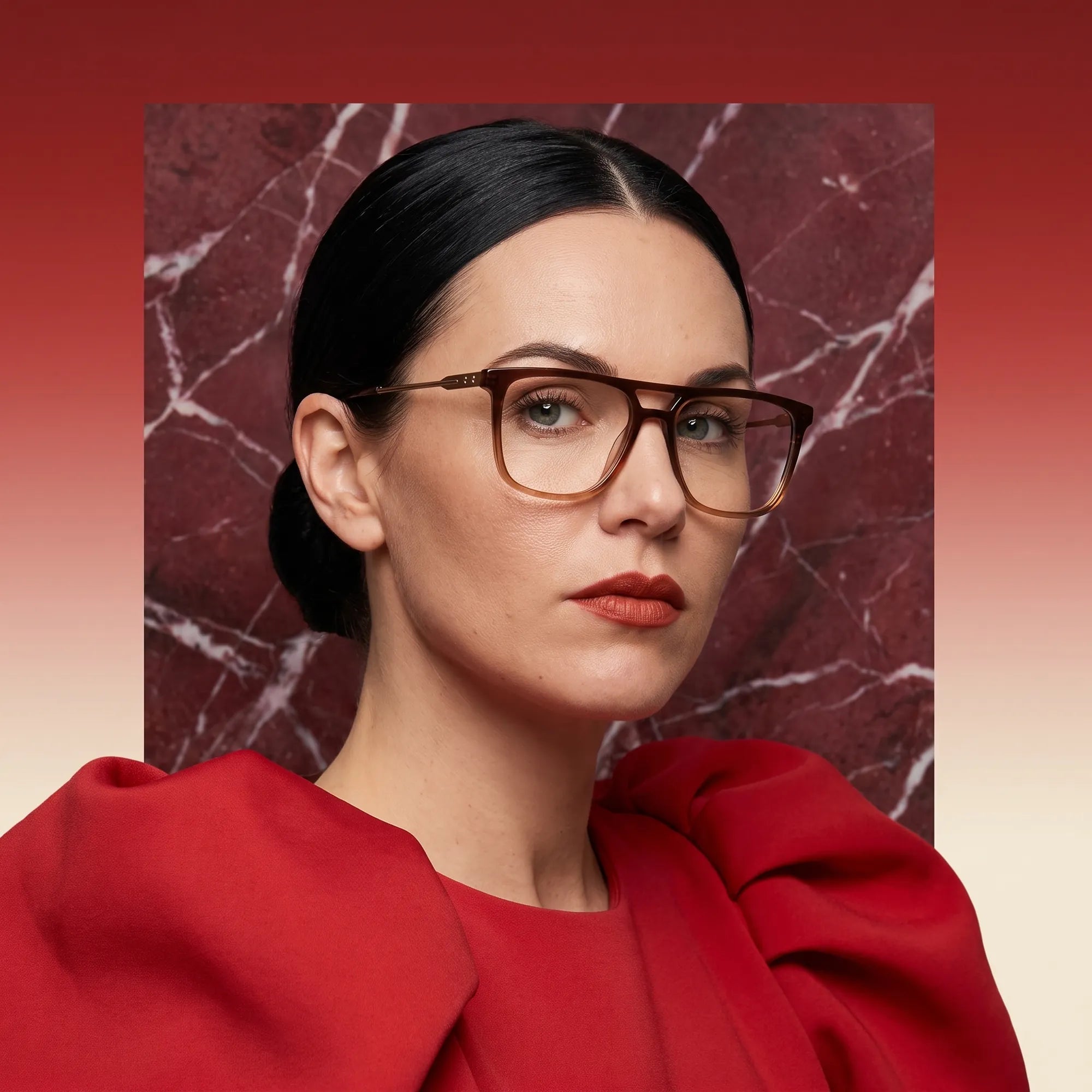 Fiore 10177 eyeglasses in brown, worn by a model – campaign portrait, red marble backdrop and draped scarlet dress