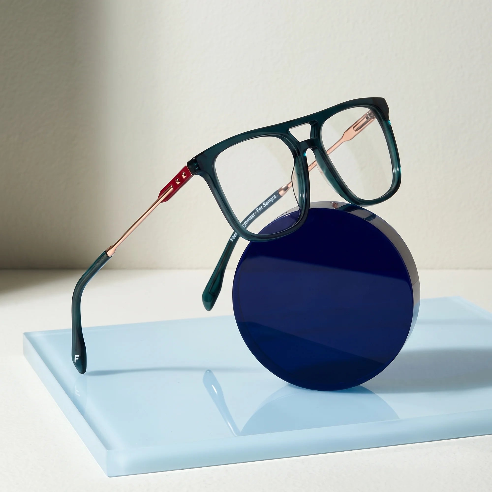 Fiore 10177 eyeglasses in green – on a cobalt acrylic disc in soft daylight