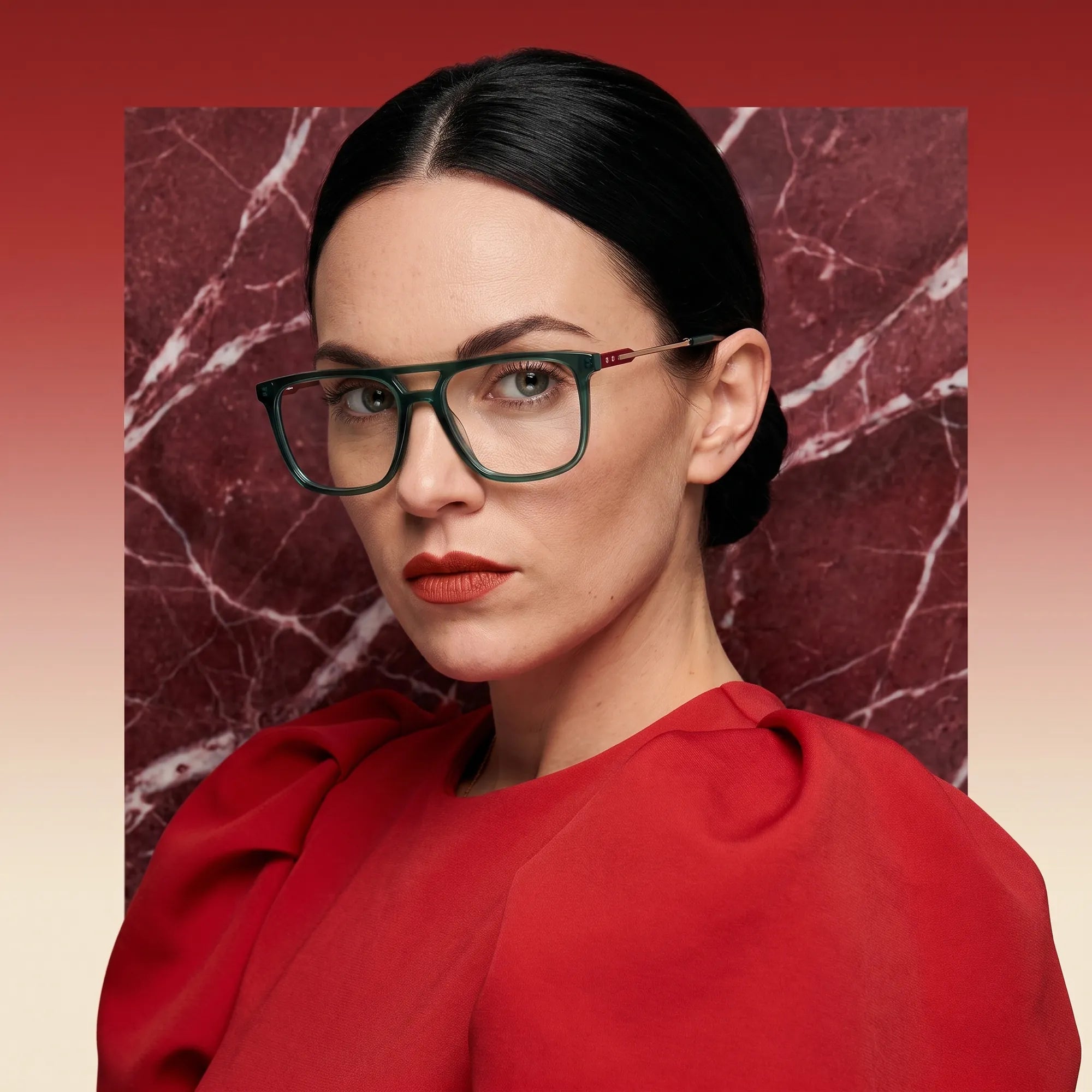 Fiore 10177 eyeglasses in green, worn by a model – campaign portrait, red marble backdrop and draped scarlet dress