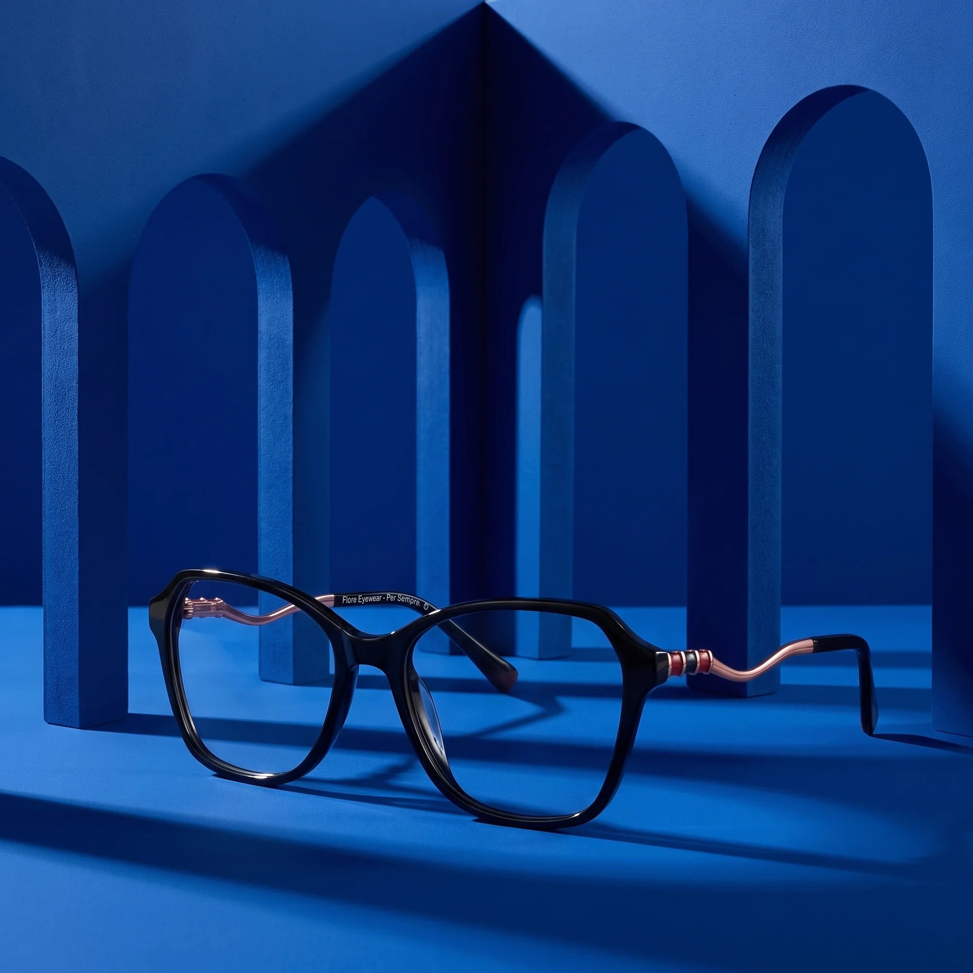 Fiore 1030 eyeglasses in black – displayed on a cobalt podium among arches