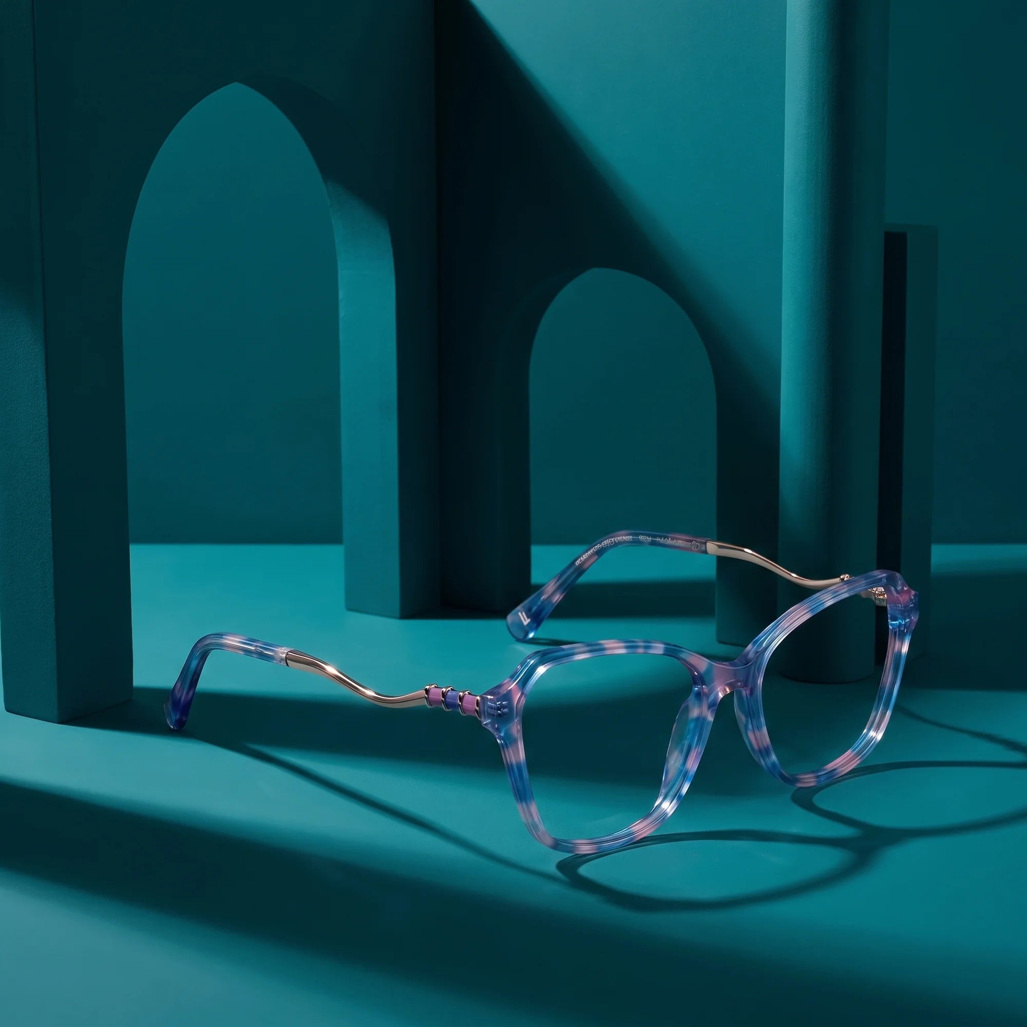 Fiore 1030 eyeglasses in blue pink – displayed on a teal podium among arches