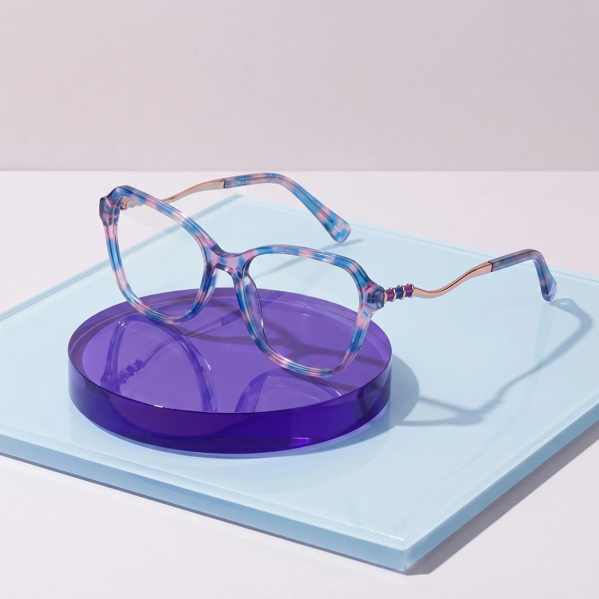 Fiore 1030 eyeglasses in blue pink – on a cobalt acrylic disc in soft daylight