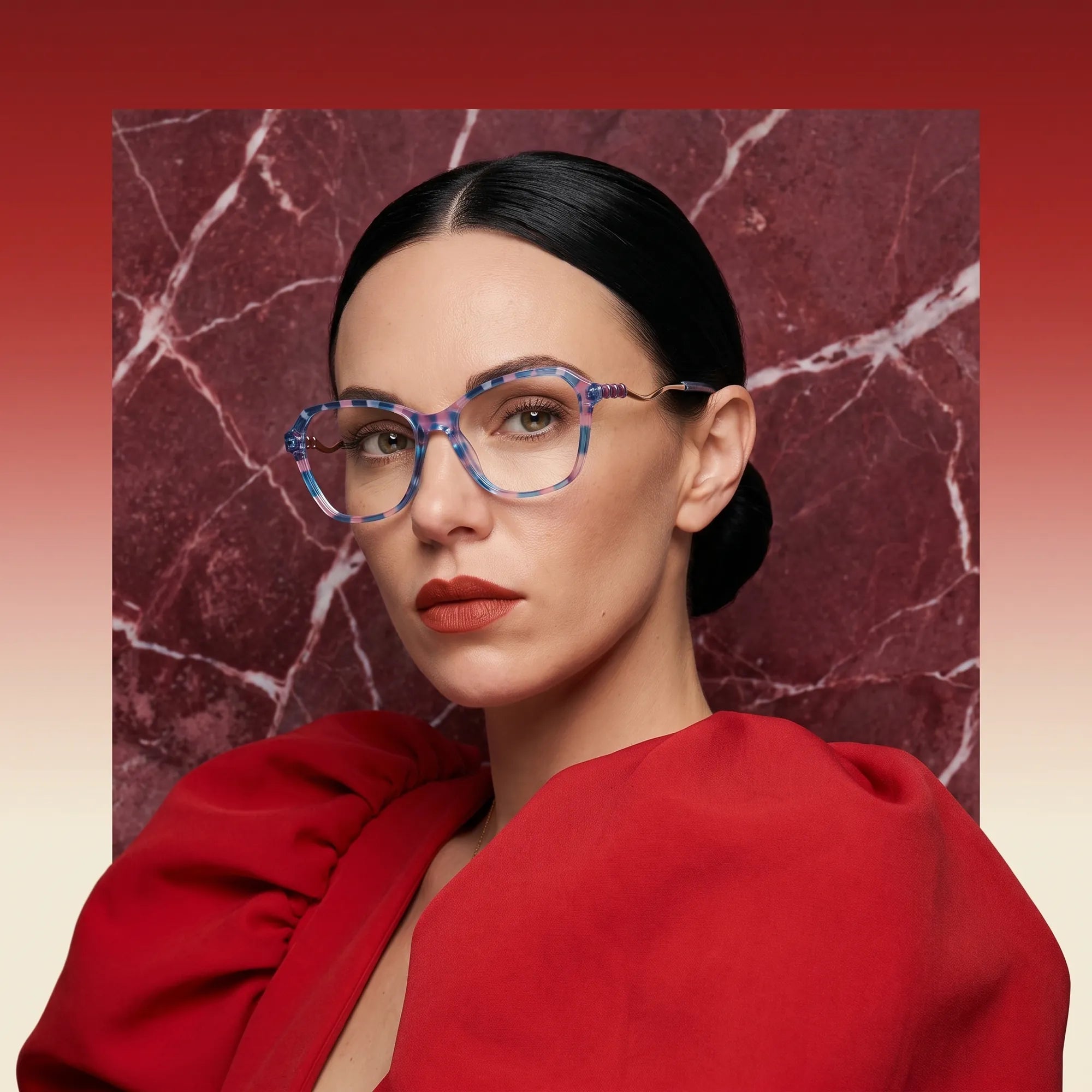 Fiore 1030 eyeglasses in blue pink, worn by a model – campaign portrait, red marble backdrop and draped scarlet dress