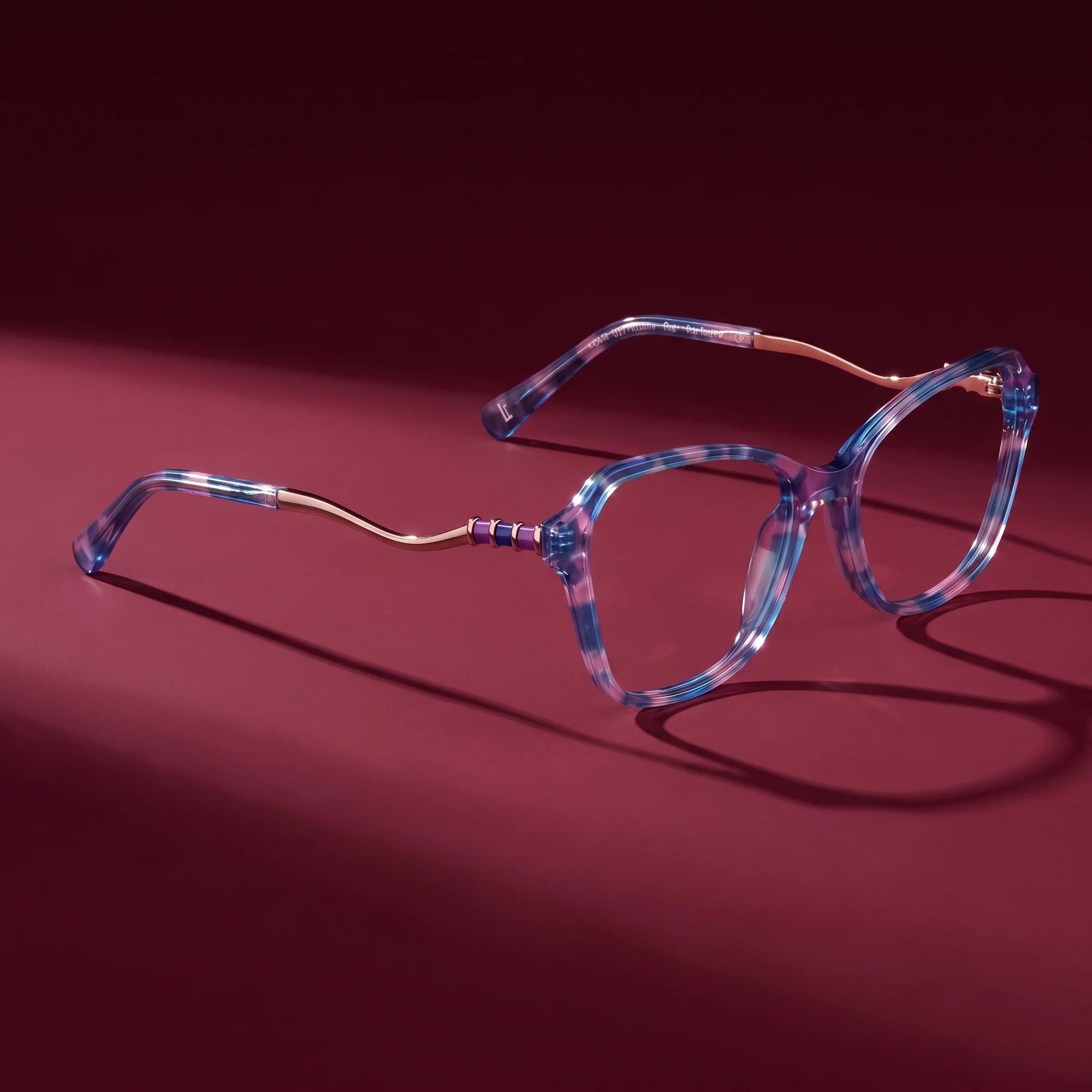Fiore 1030 eyeglasses in blue pink – hero still life against a deep burgundy backdrop