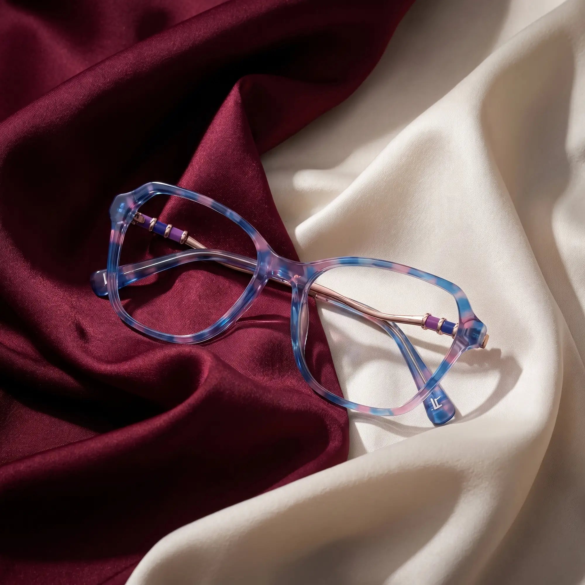 Fiore 1030 eyeglasses in blue pink – resting on draped burgundy and ivory silk