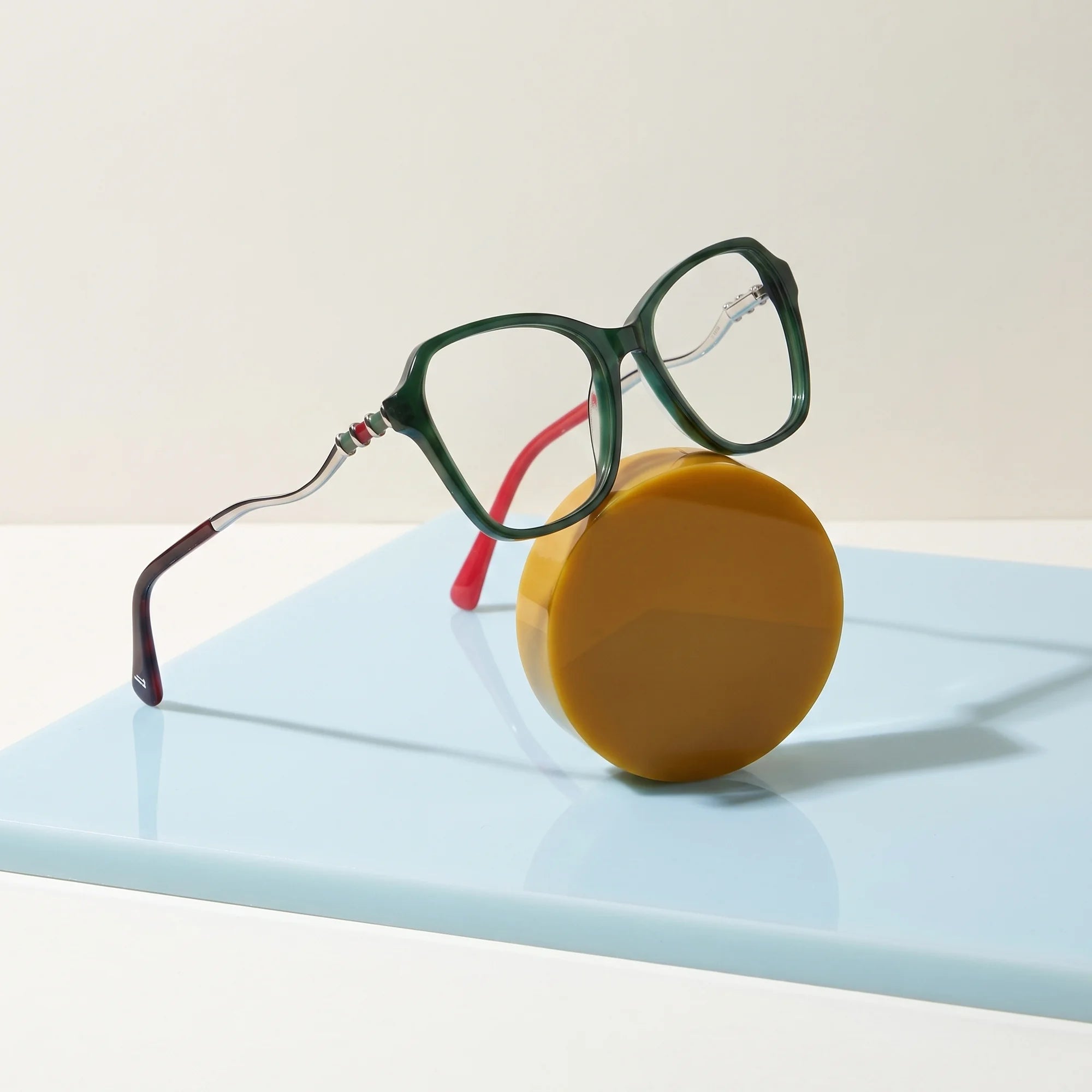 Fiore 1030 eyeglasses in green – on a cobalt acrylic disc in soft daylight