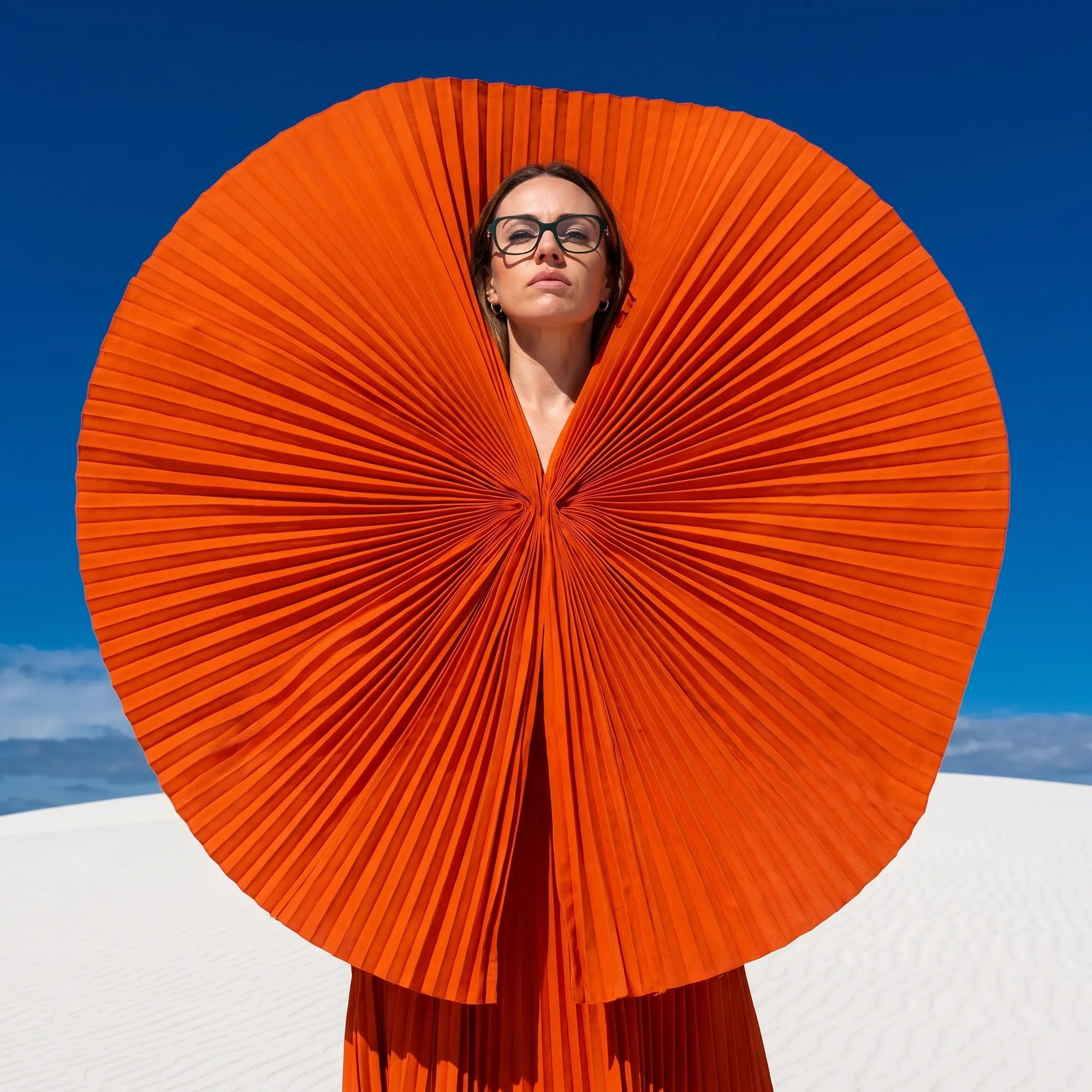 Fiore 1030 eyeglasses in green, worn by a model – campaign portrait, sculptural orange pleated fan on white dunes
