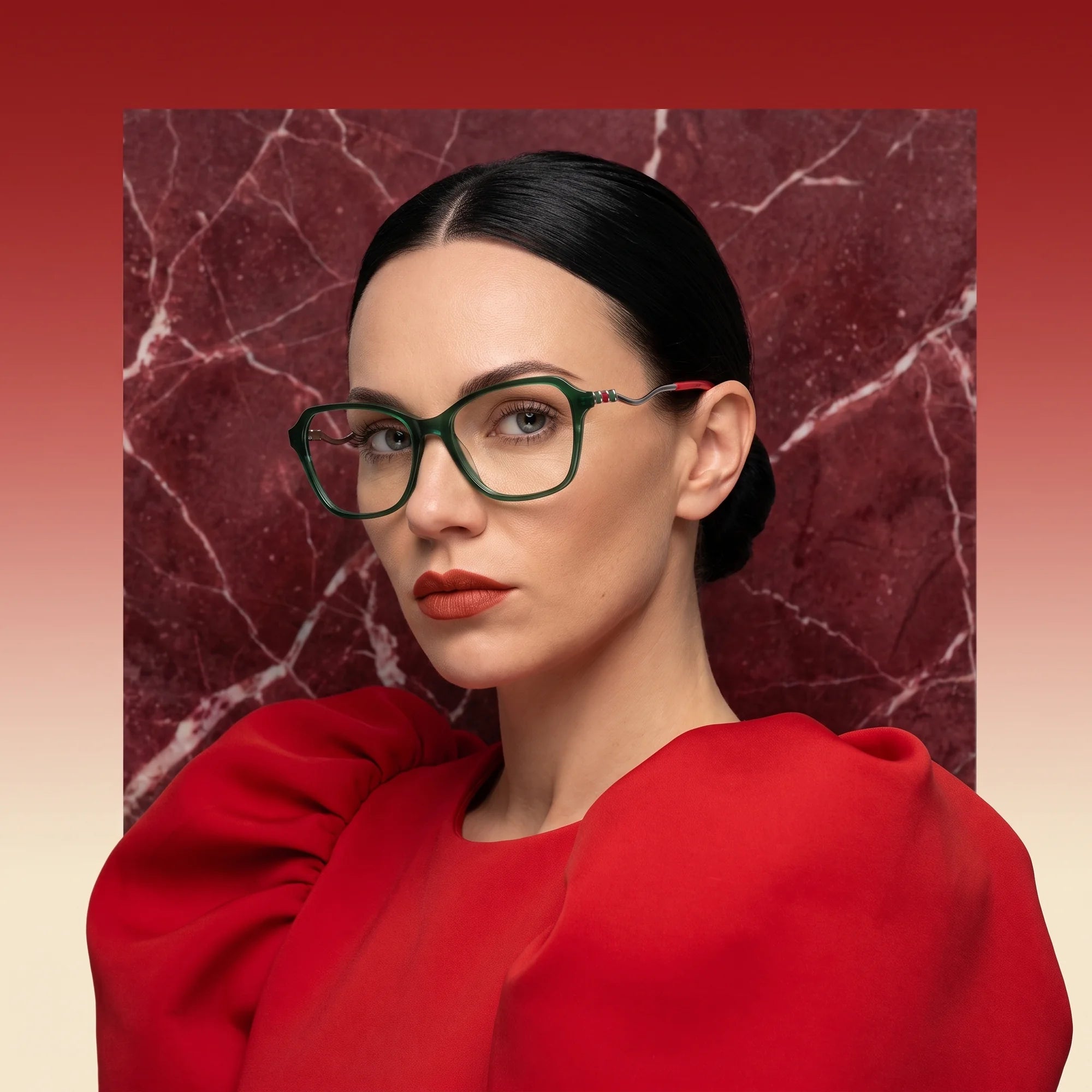 Fiore 1030 eyeglasses in green, worn by a model – campaign portrait, red marble backdrop and draped scarlet dress