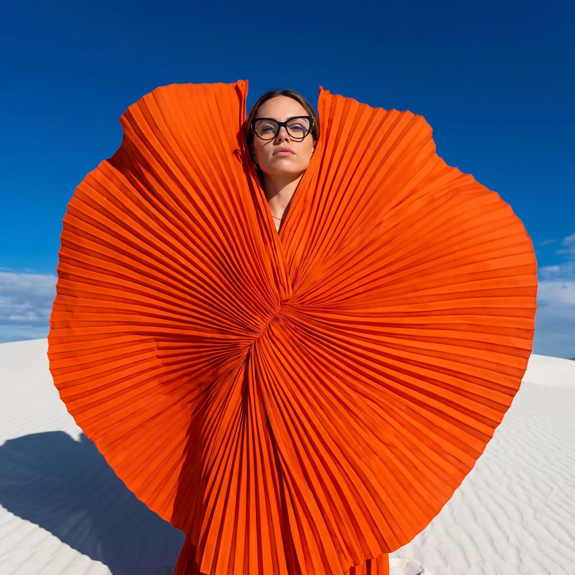 Fiore 1031 eyeglasses in black, worn by a model – campaign portrait, sculptural orange pleated fan on white dunes