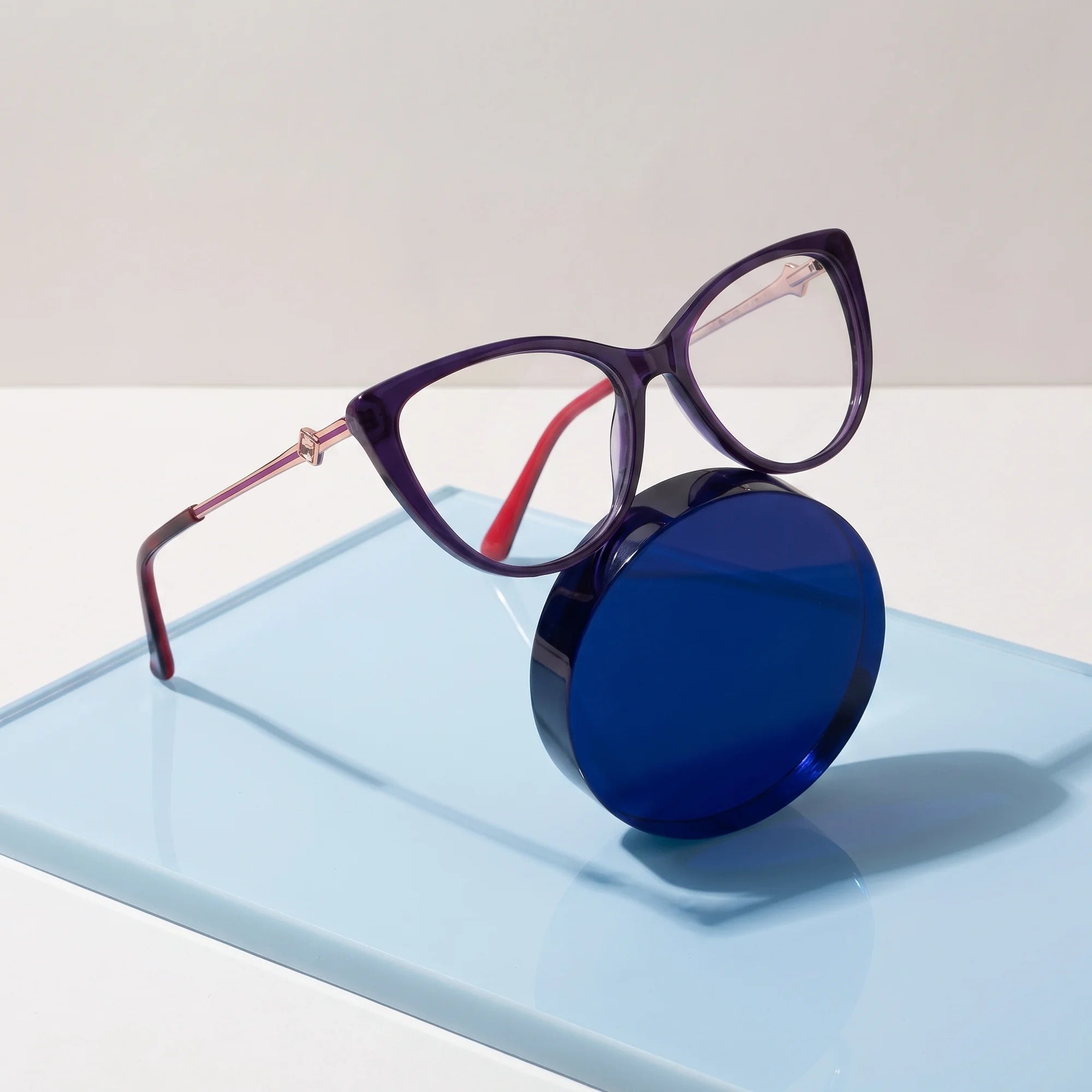 Fiore 1031 eyeglasses in purple green – on a cobalt acrylic disc in soft daylight