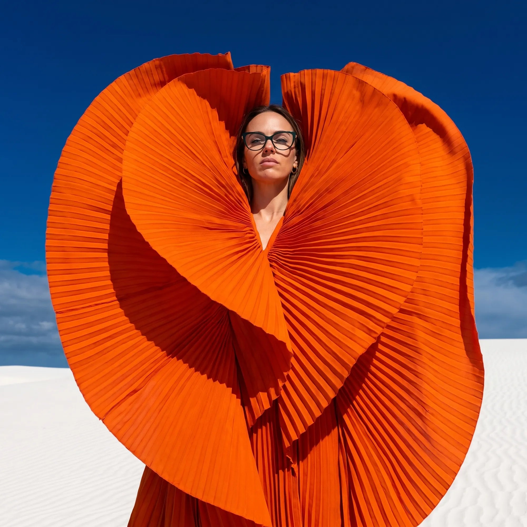 Fiore 1031 eyeglasses in green, worn by a model – campaign portrait, sculptural orange pleated fan on white dunes