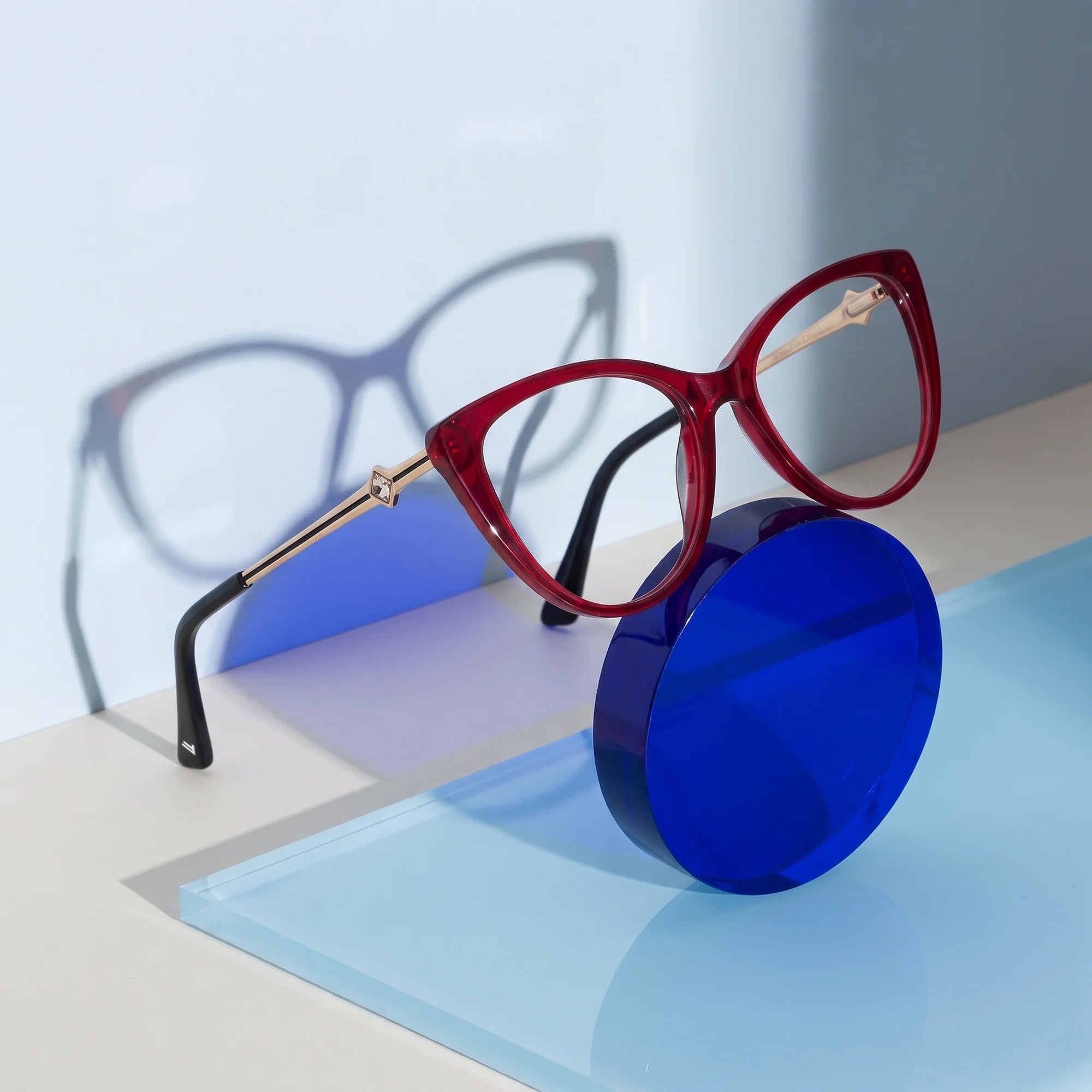 Fiore 1031 eyeglasses in red – on a cobalt acrylic disc in soft daylight