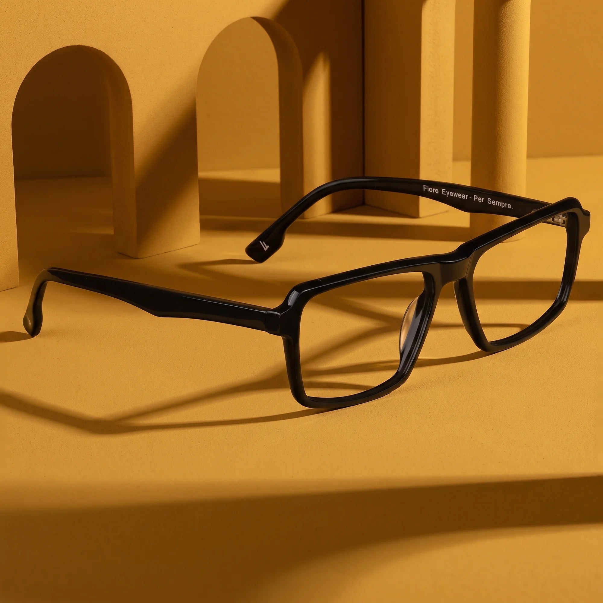 Fiore 1038 eyeglasses in black – displayed on a mustard ochre podium among arches