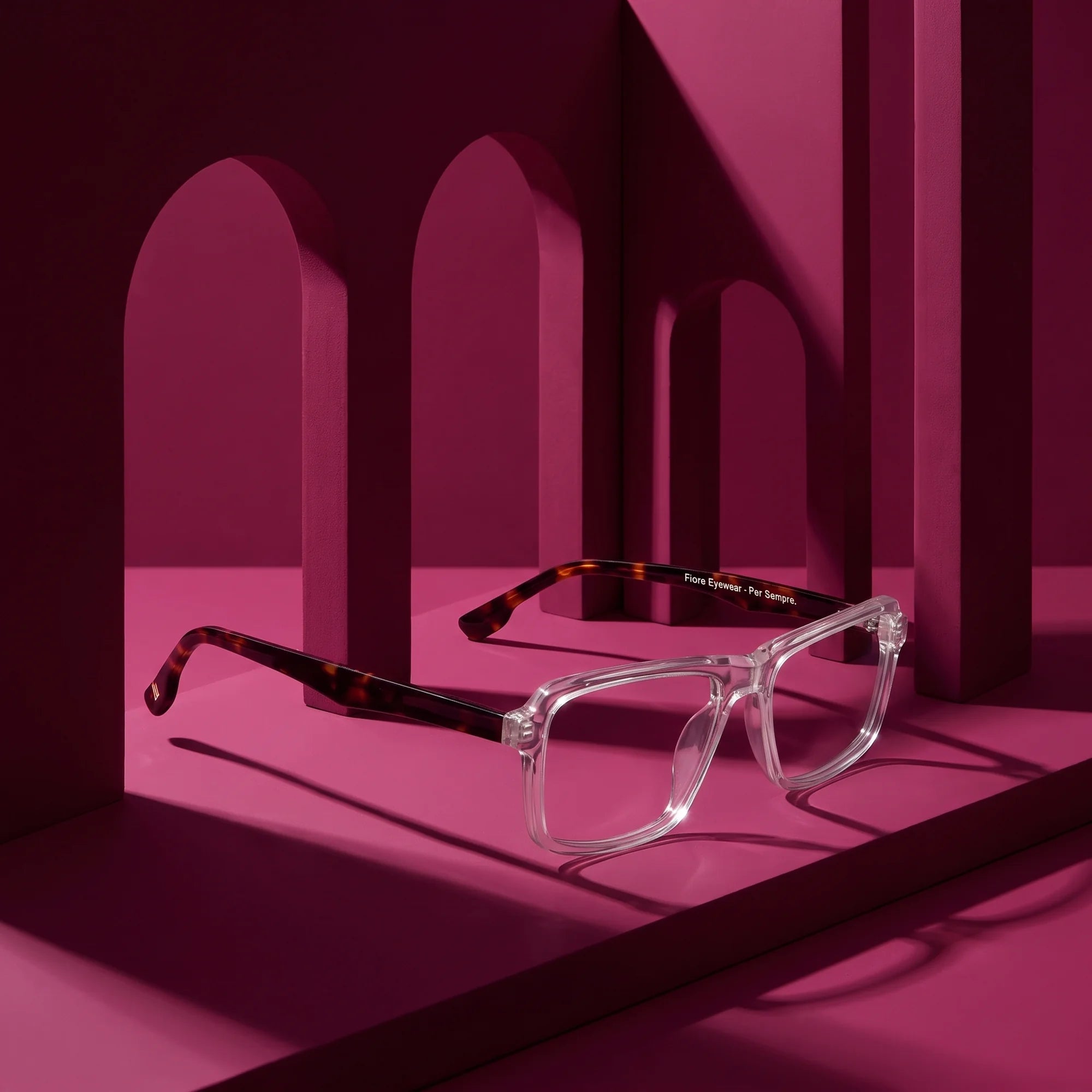 Fiore 1038 eyeglasses in transparent – displayed on a magenta podium among arches