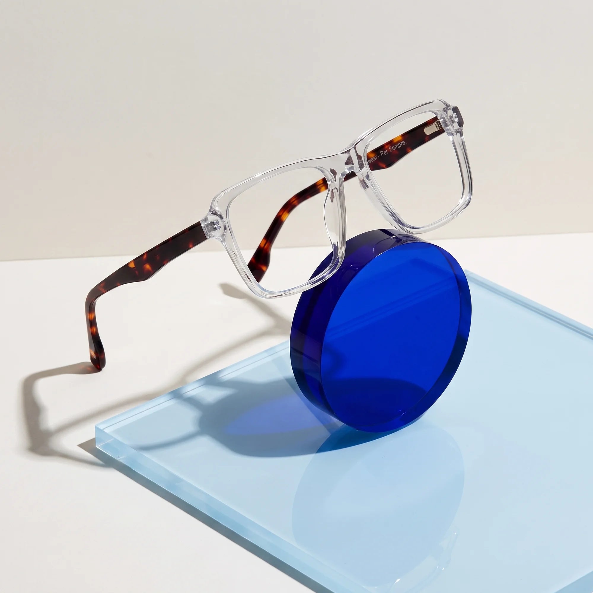 Fiore 1038 eyeglasses in transparent – on a cobalt acrylic disc in soft daylight