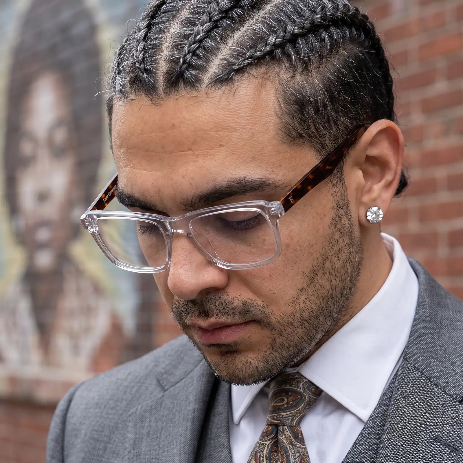 Fiore 1038 eyeglasses in transparent, worn by a model – campaign portrait, pensive portrait against a painted brick mural