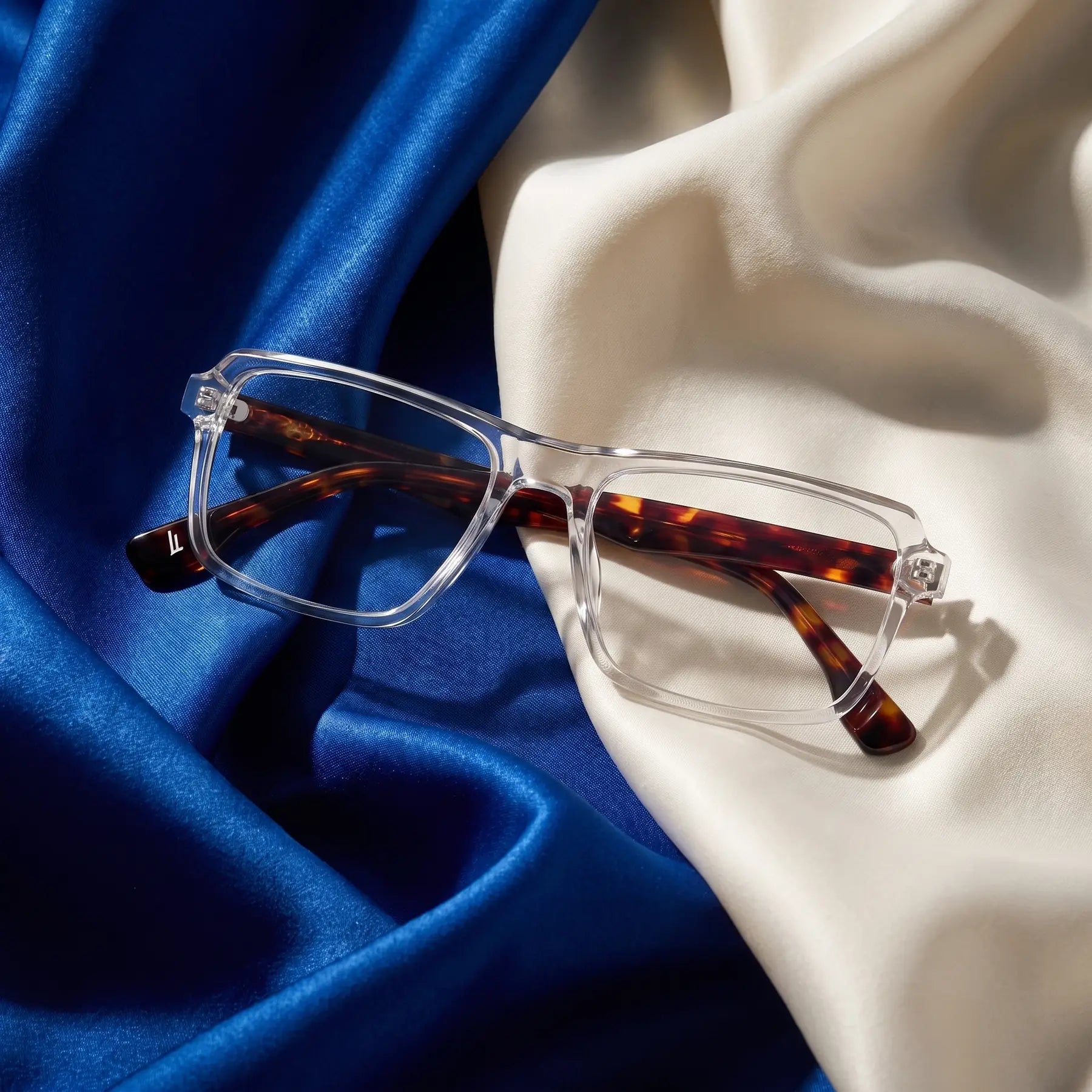 Fiore 1038 eyeglasses in transparent – resting on draped cobalt and ivory silk