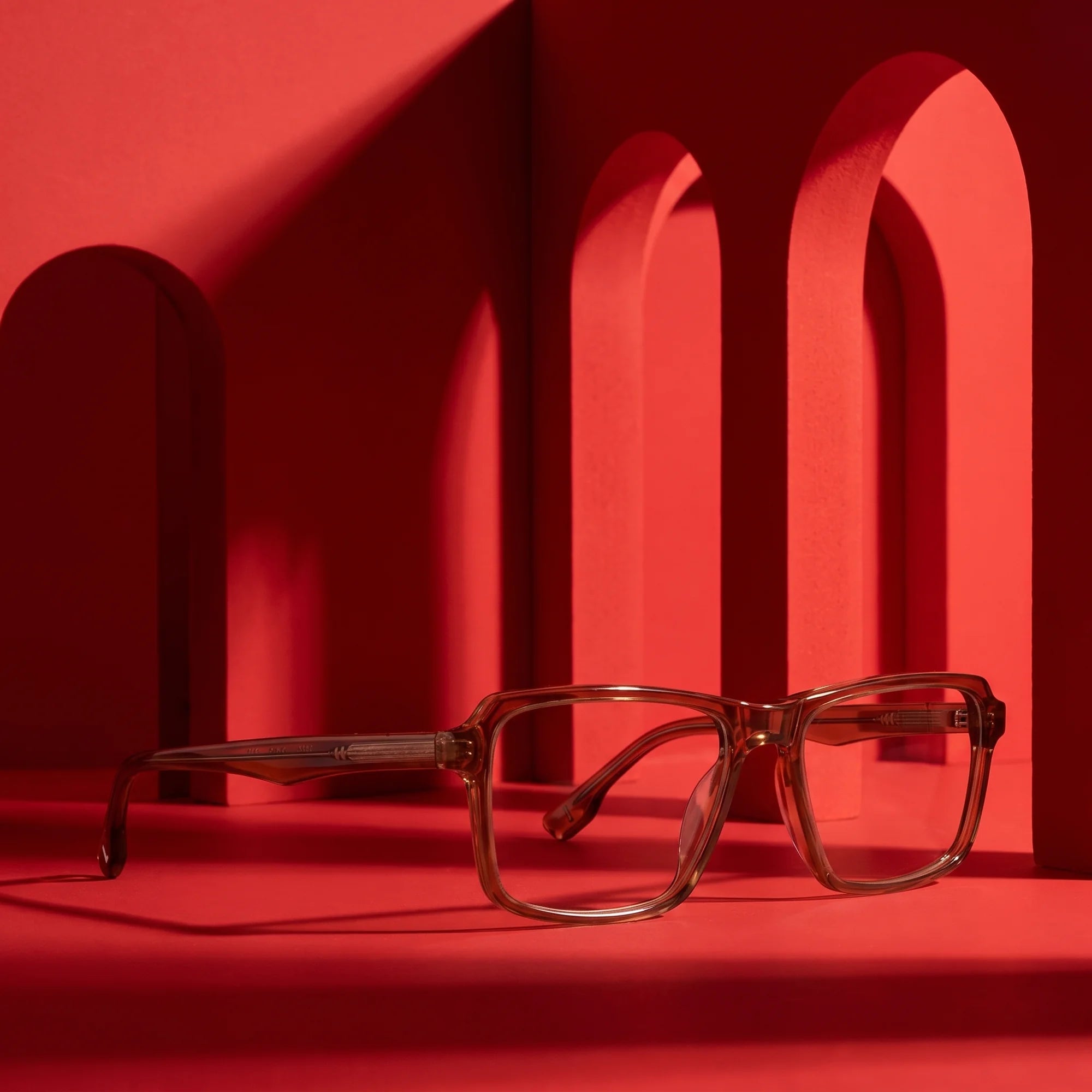 Fiore 1038 eyeglasses in brown – displayed on a vivid red podium among arches