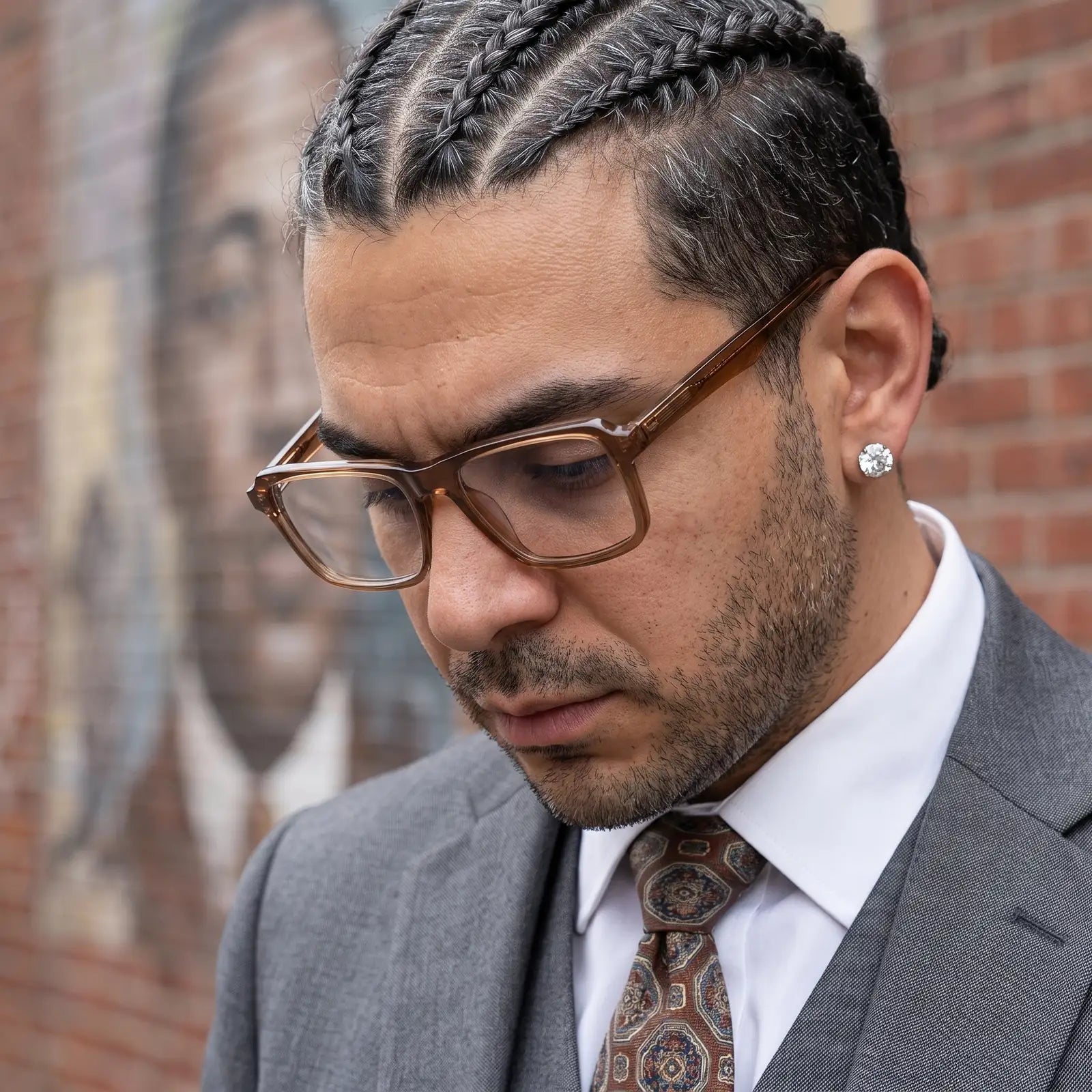 Fiore 1038 eyeglasses in brown, worn by a model – campaign portrait, pensive portrait against a painted brick mural