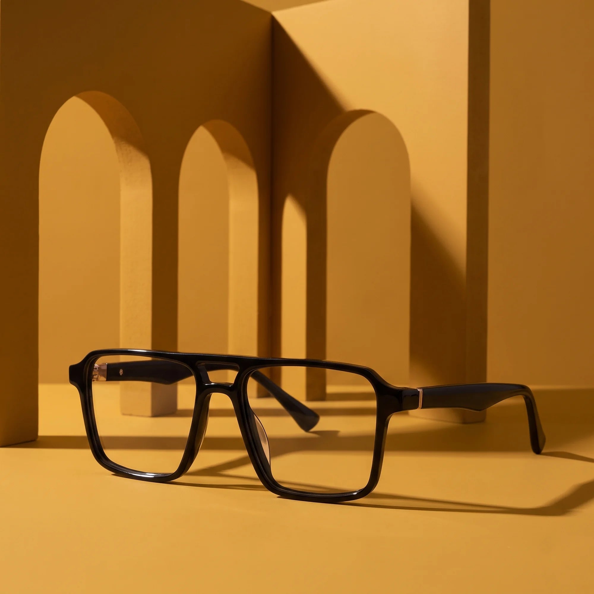 Fiore 1039 eyeglasses in black – displayed on a mustard ochre podium among arches